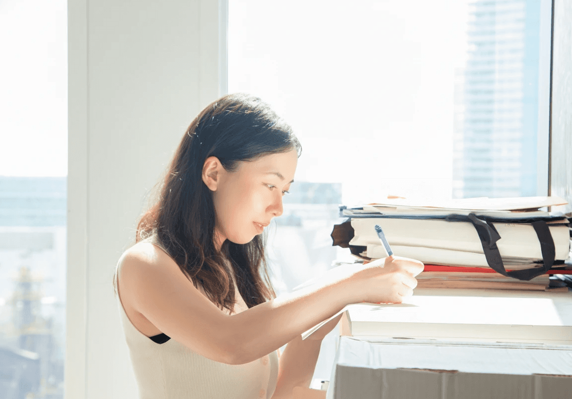 Female looking right, rests hands on table, writing