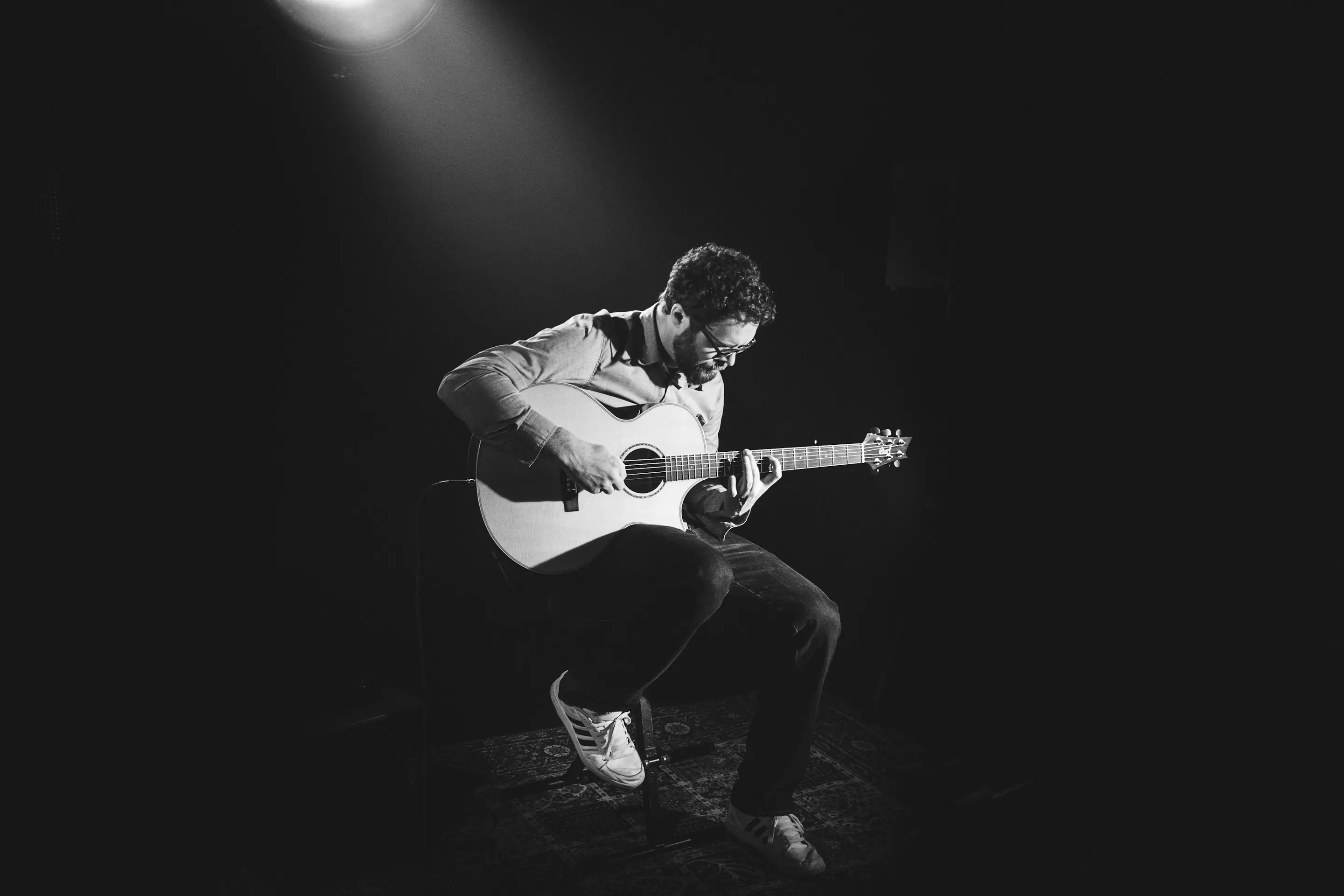 A guitarist playing on a dark stage, in black and white