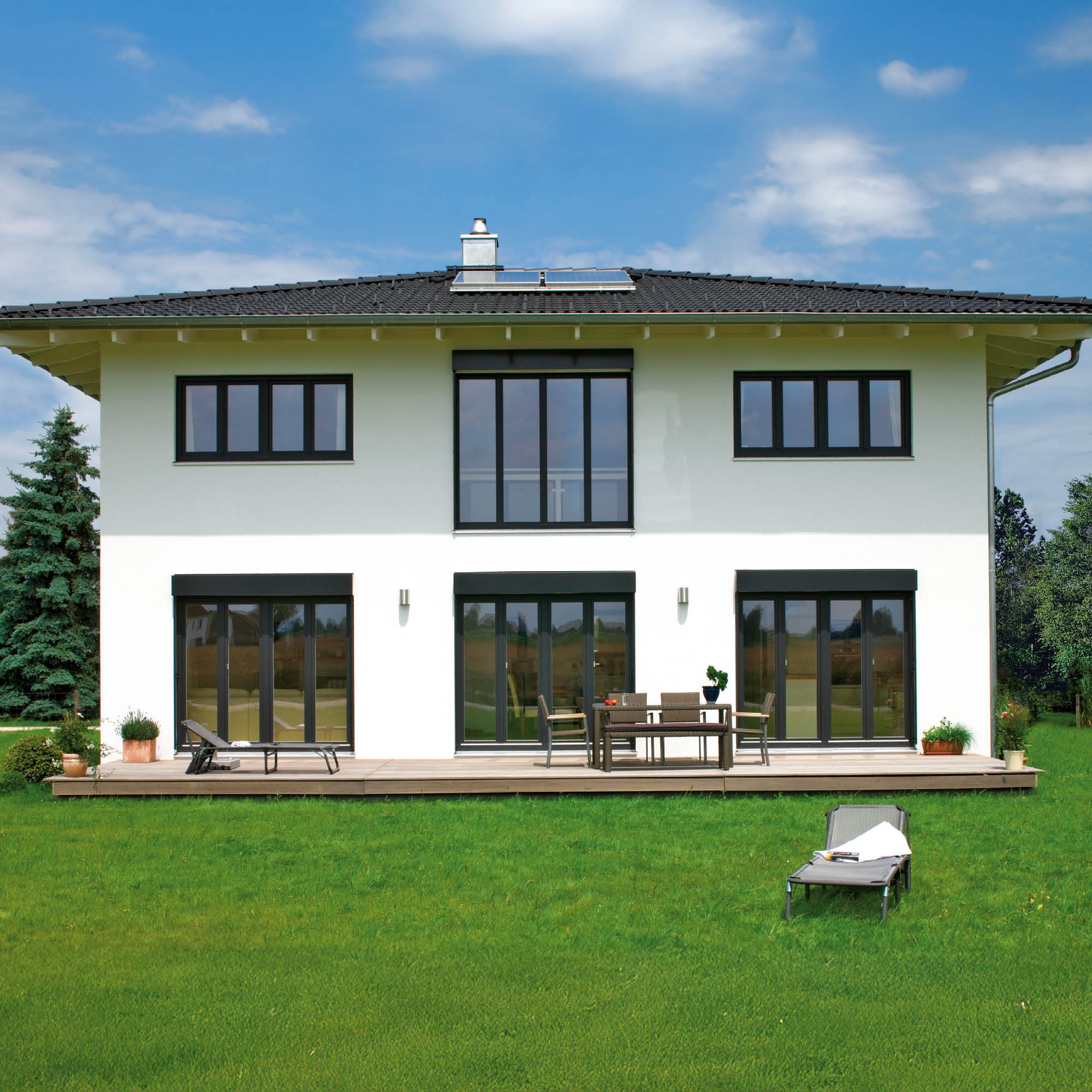 Modernes weißen Haus mit großen Glasflächen, Dachterrasse und gepflegtem Garten unter blauem Himmel.