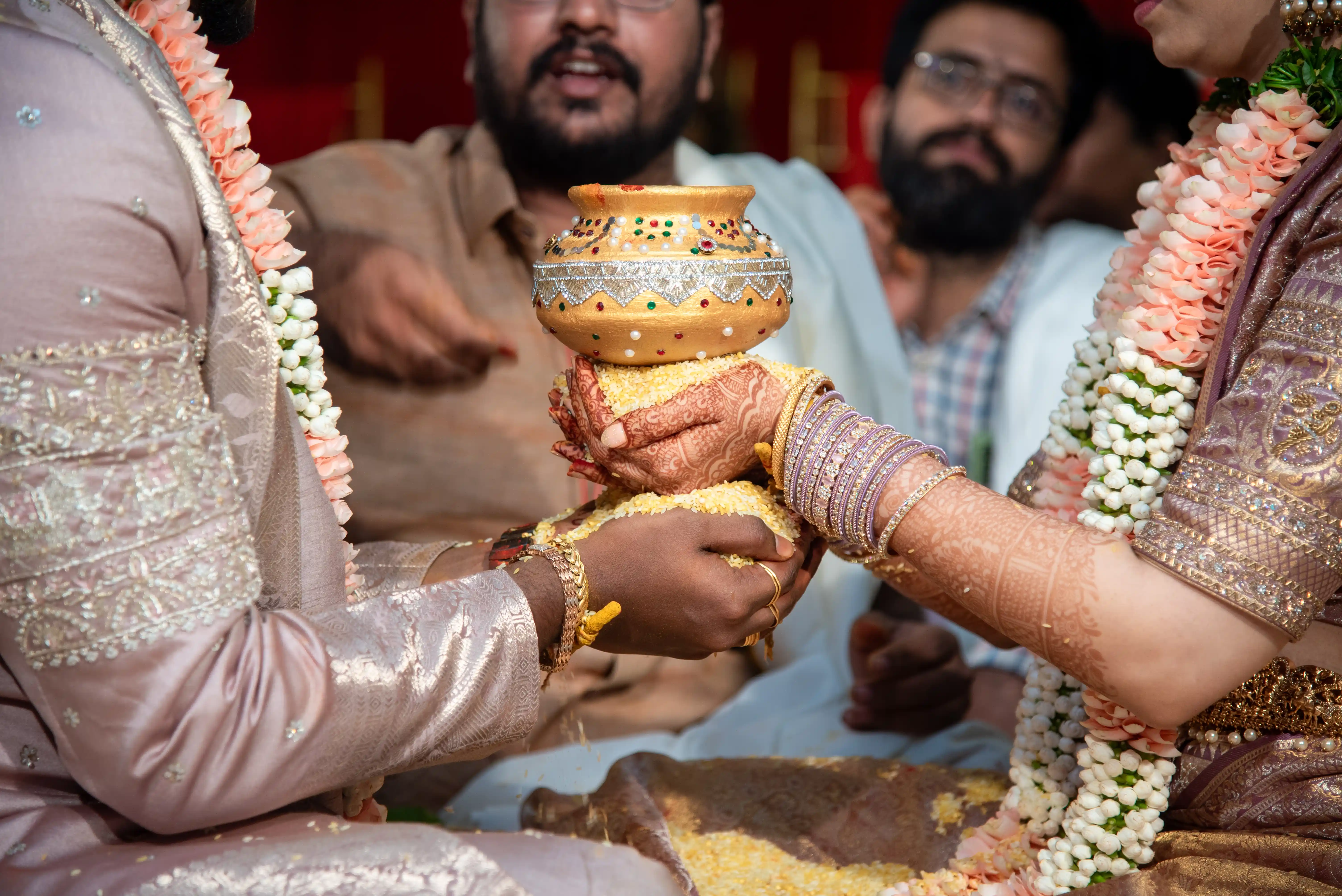 Detail shot of bride and groom's hands holding a decorative pot in a symbolic rice ceremony, illustrating the elegance and spirituality of traditional wedding customs, captured by Out of The Blues Fine Art Wedding Photography in Hyderabad.