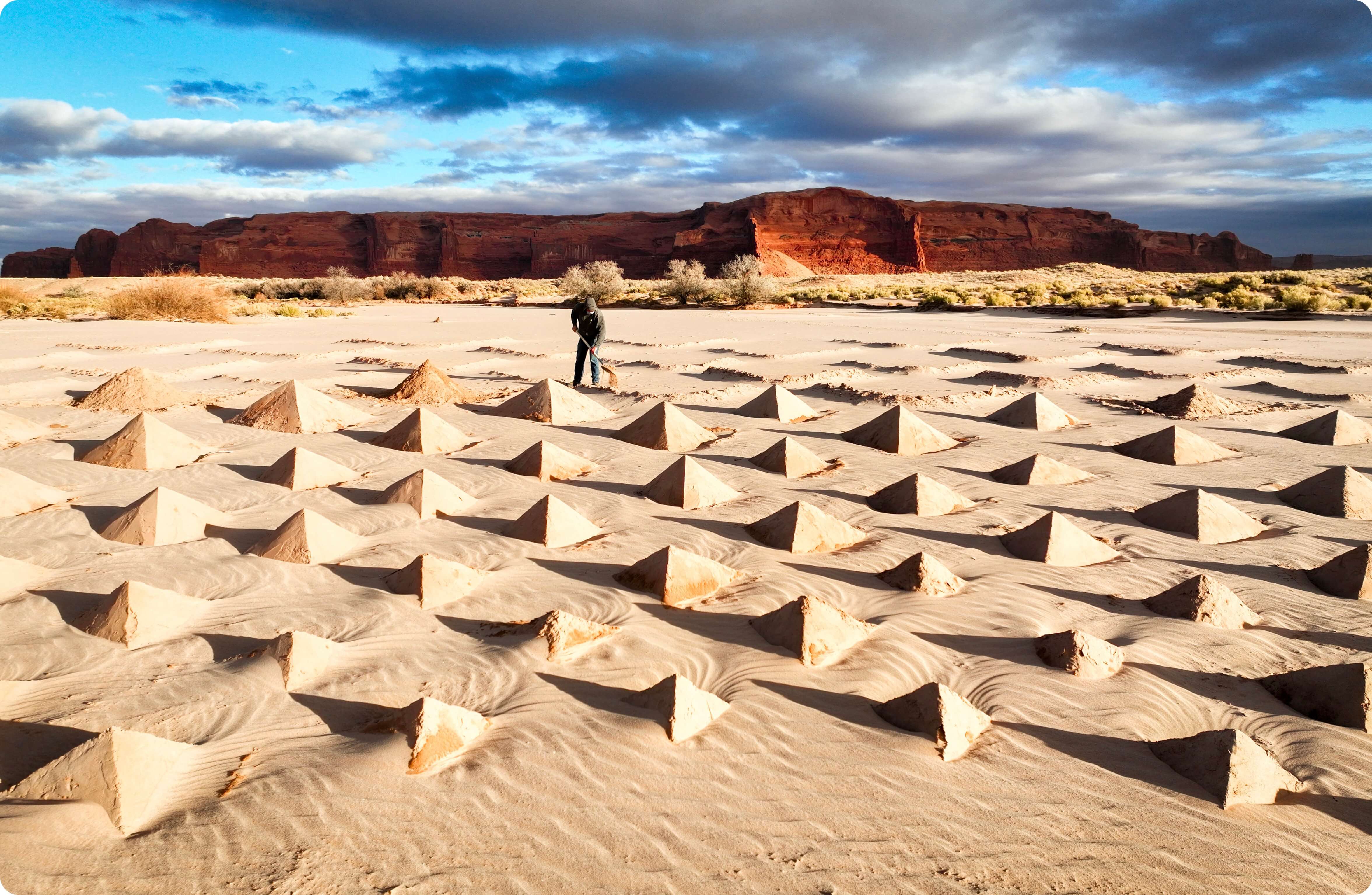 A man digging in the sand to build a massive piece of land art in a riverbed in front of Arizona red rocks