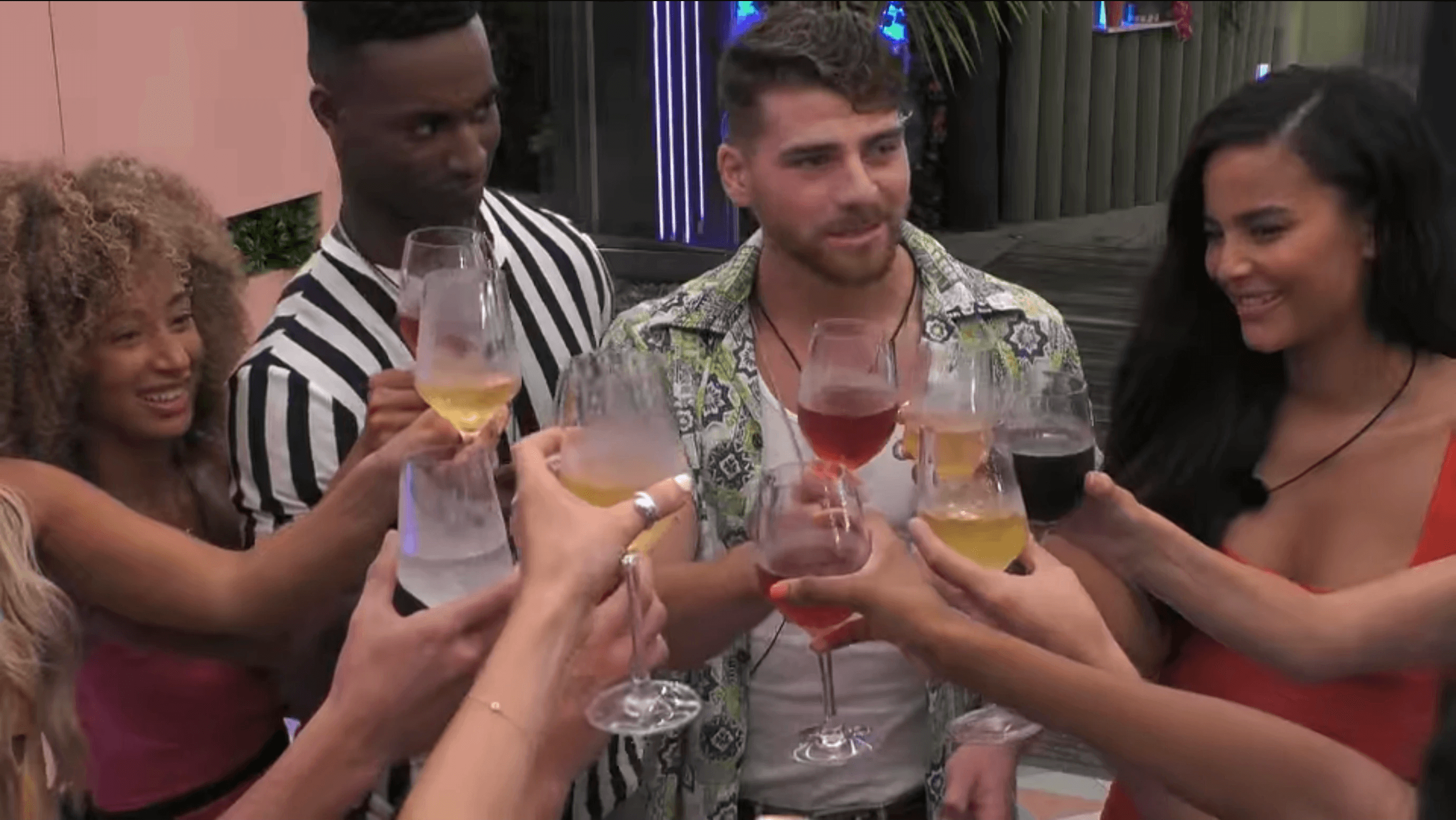 Young men and women raising their glasses, and a man in the center of the frame is giving a toast.