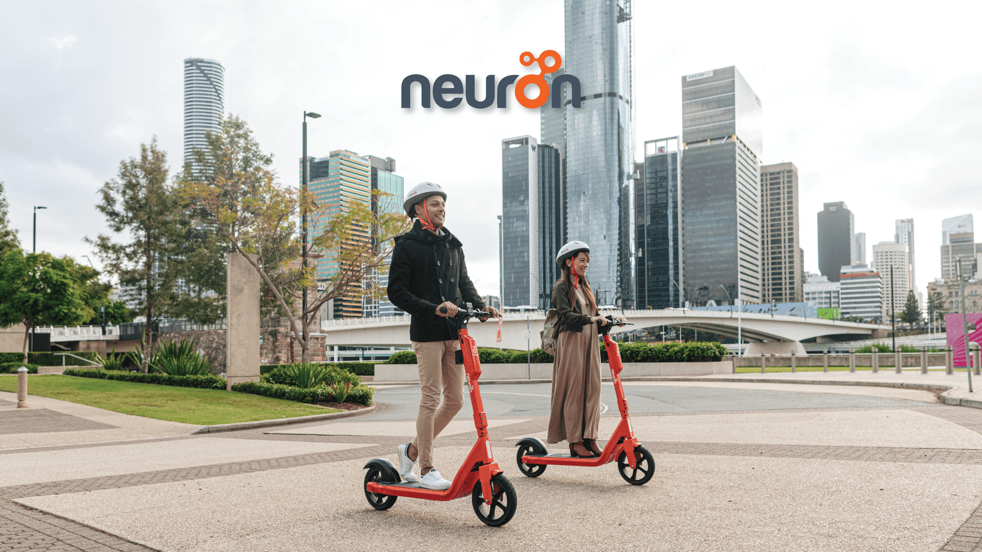 Two helmeted Neuron e-scooter riders in an urban setting