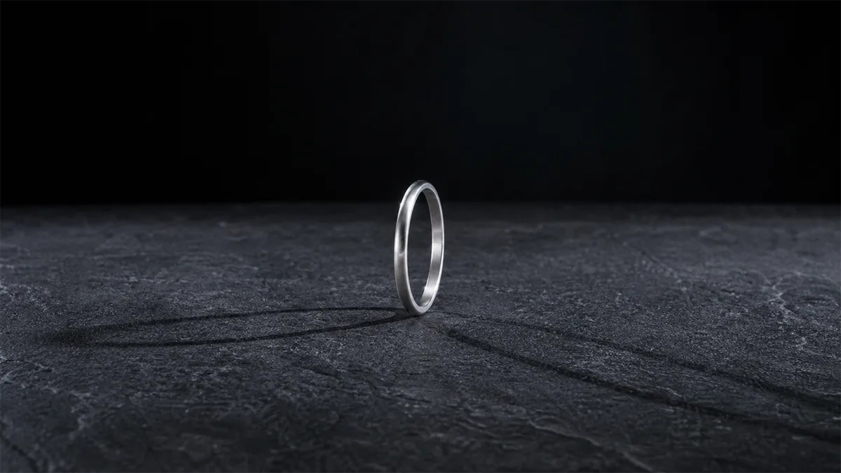 Plain silver-toned ring casting two opposing shadows across a dark stone surface