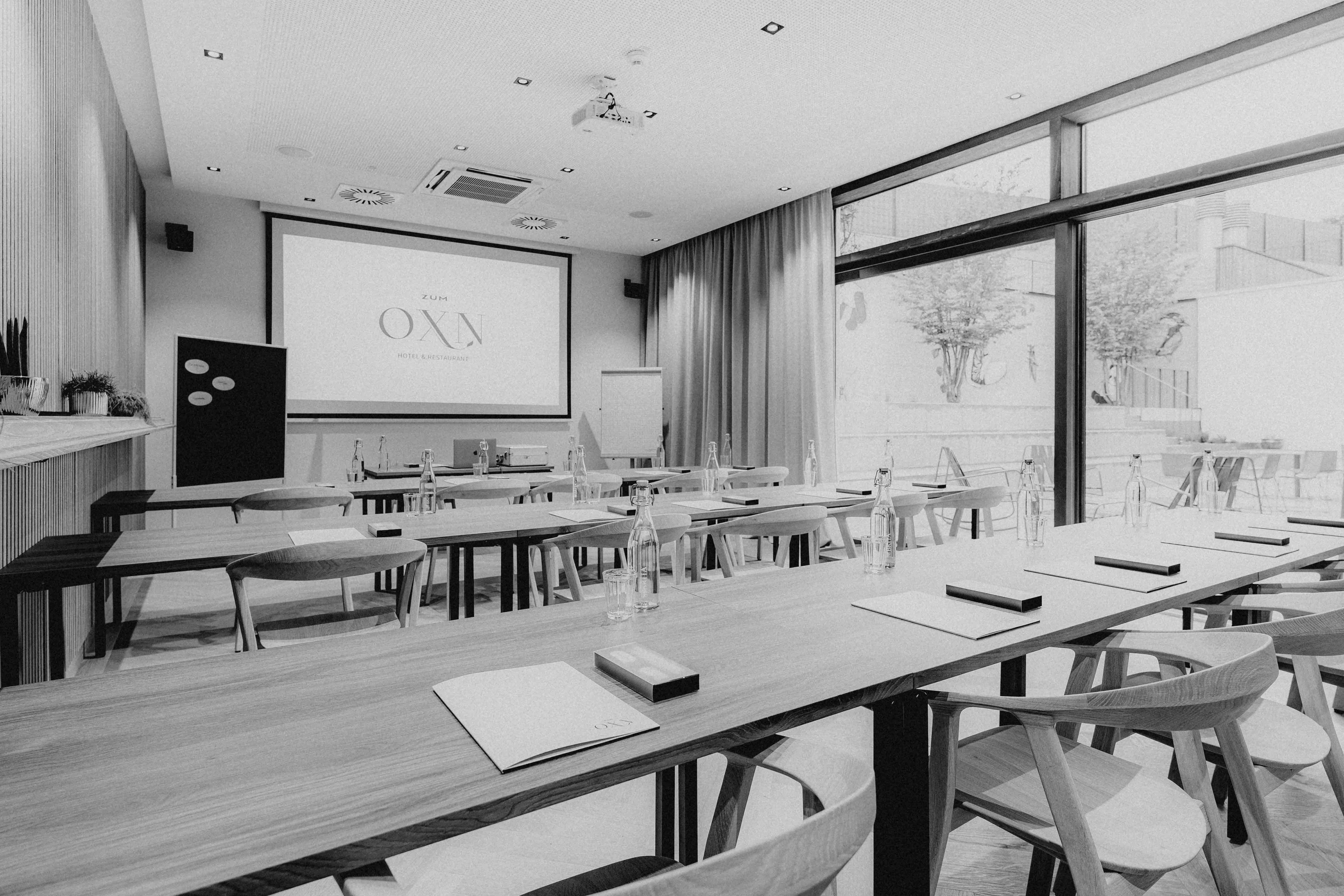 A modern classroom in black and white, featuring desks, a large screen, and windows with natural light.