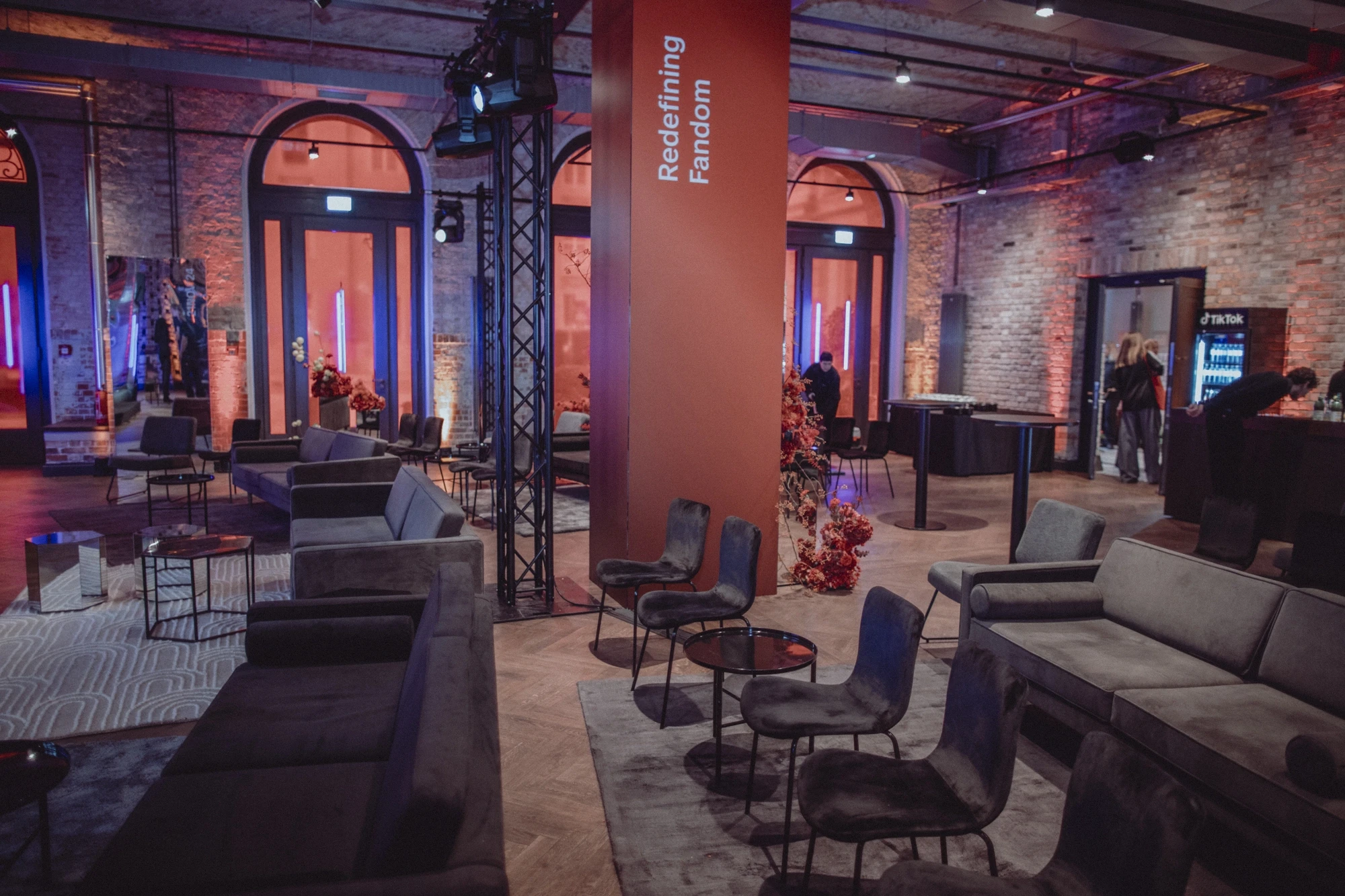 Seating areas with grey chairs and sofas around the Redefining Fandom pillar in red light.
