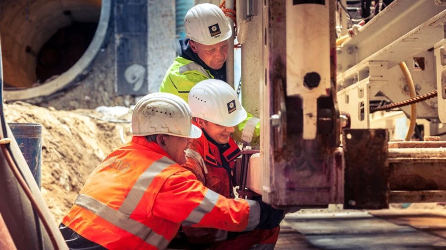 Bauarbeiter in Sicherheitsausrüstung arbeiten vor Ort zusammen und inspizieren Maschinen innerhalb eines Tunnelprojekts.