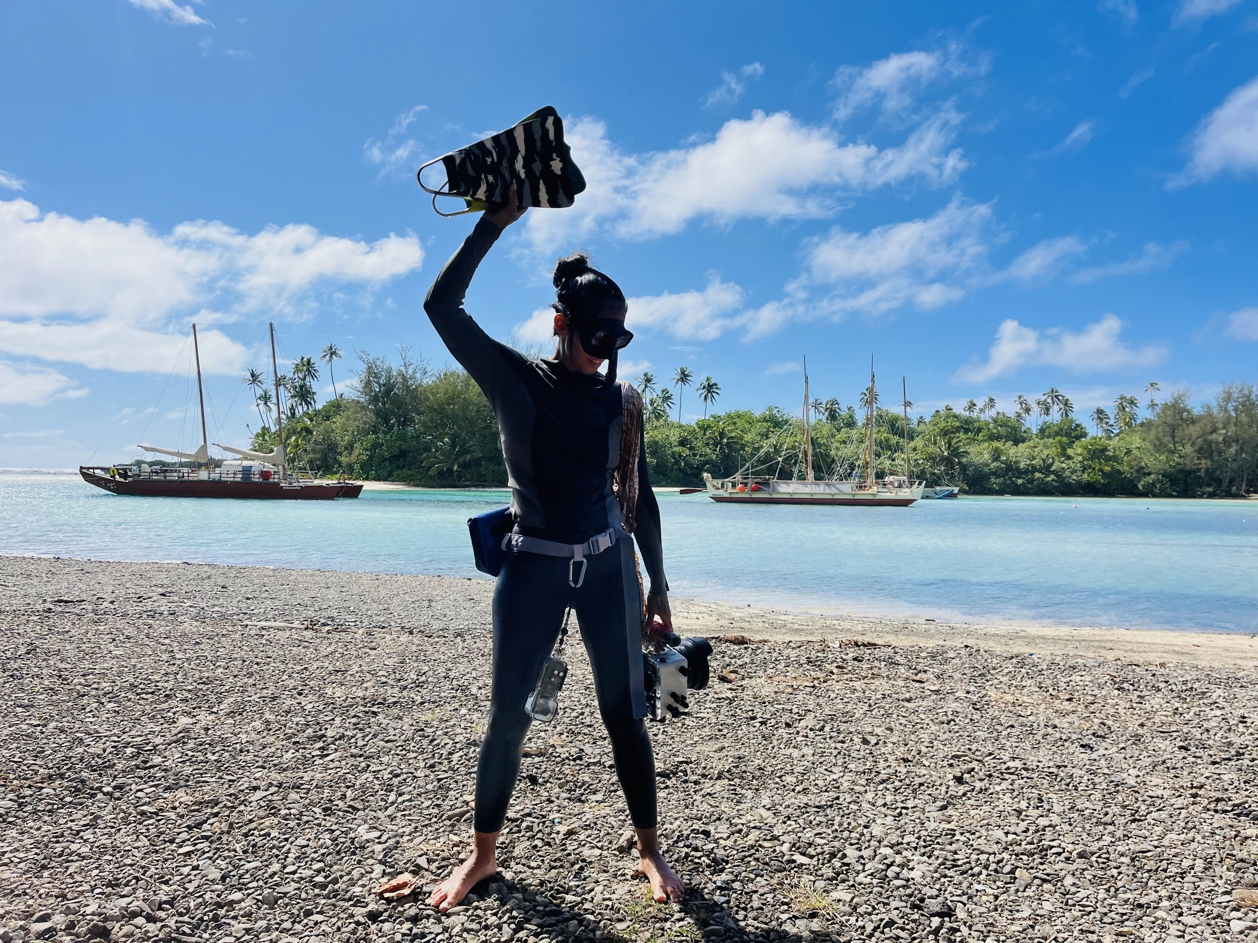 A woman in black stands focused over a laptop on a table, surrounded by colorful paper samples pinned to a white wall, creating an artistic, thoughtful atmosphere.