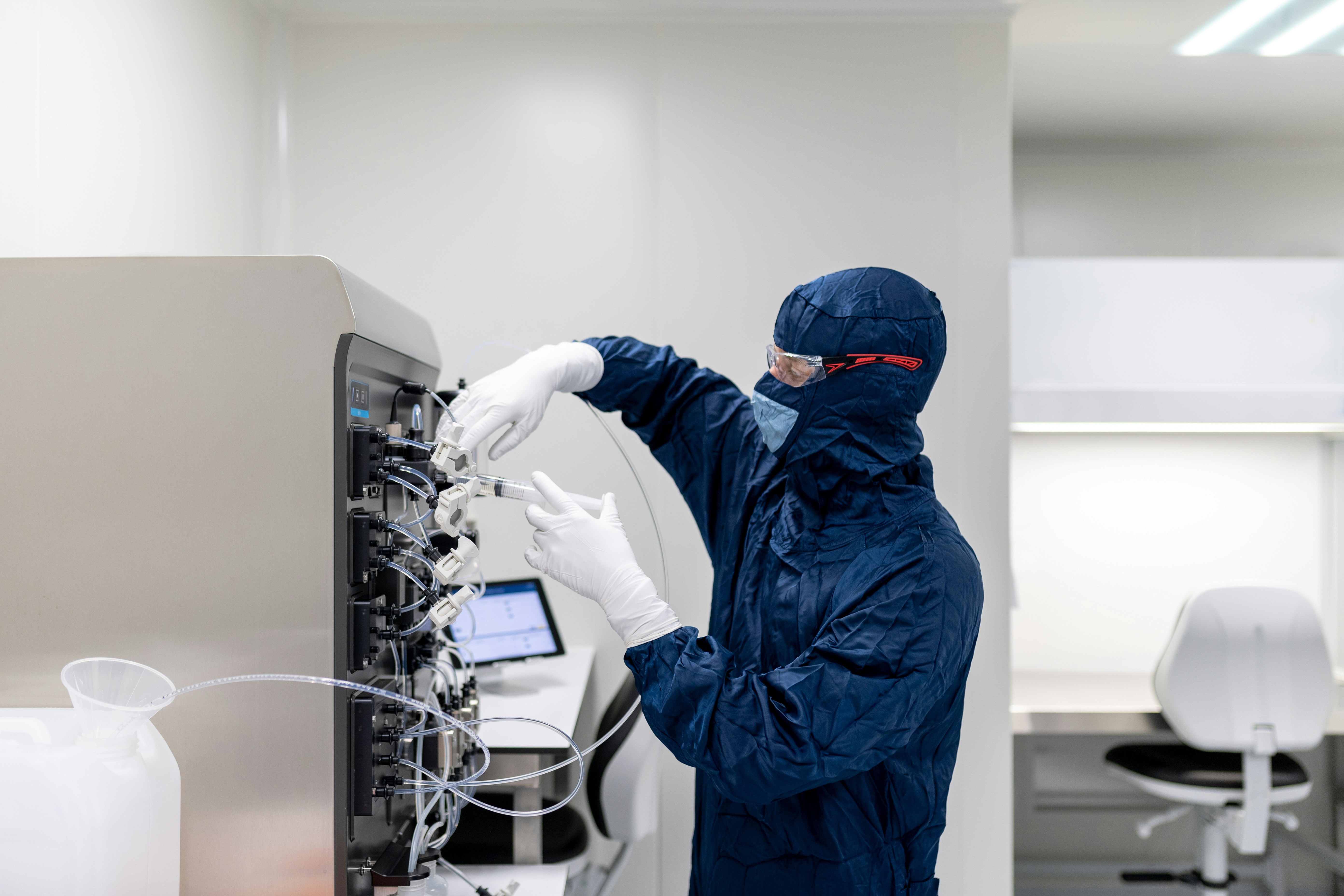 Close-up of a scientist holding a tray of petri dishes with purple cultures, wearing gloves and safety gear.