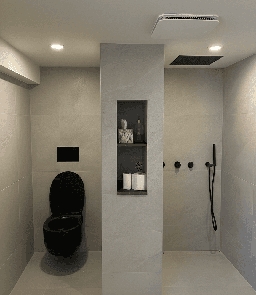Salle de bain très minimaliste dans les tons de gris chaud. Une colonne centrale sépare deux zones. À gauche, il y a une toilette murale noire et à droite, il y a une douche sans vitre avec de la plomberie noire. La colonne comporte un alcôve intégré à la vertical avec une tablette au milieu, idéale pour accueillir les produits.
