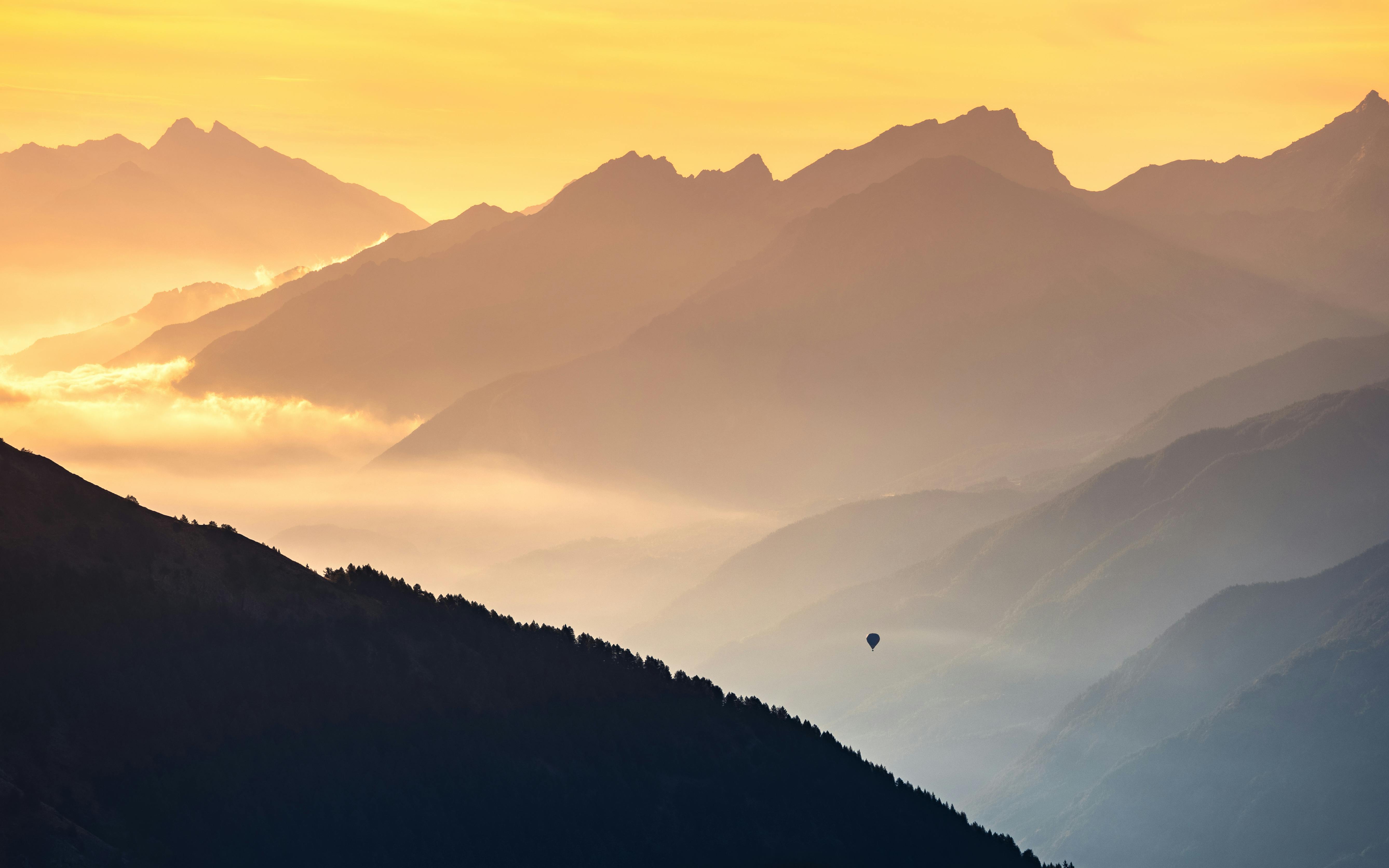 a hot air balloon flies among the mountains at dawn