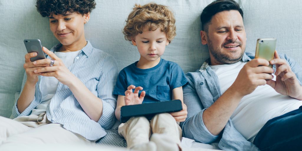 a man, woman and child sitting on a couch looking at their cell phones