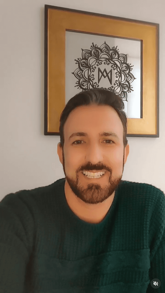 Smiling female therapist with short gray hair, wearing a brown top and a purple shawl, surrounded by a cozy background.