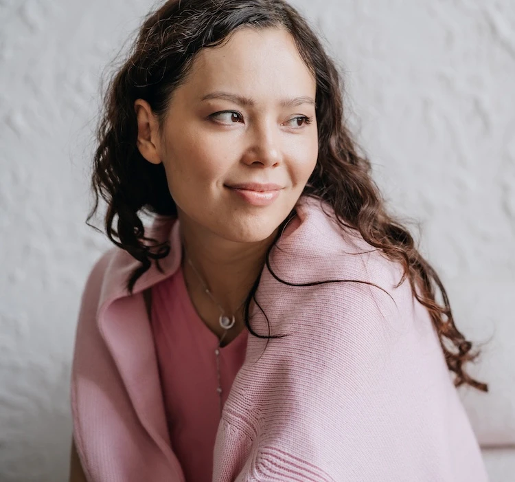 Smiling Kristina Lo therapist with long brown hair, wearing a purple shawl, surrounded by a cozy background.