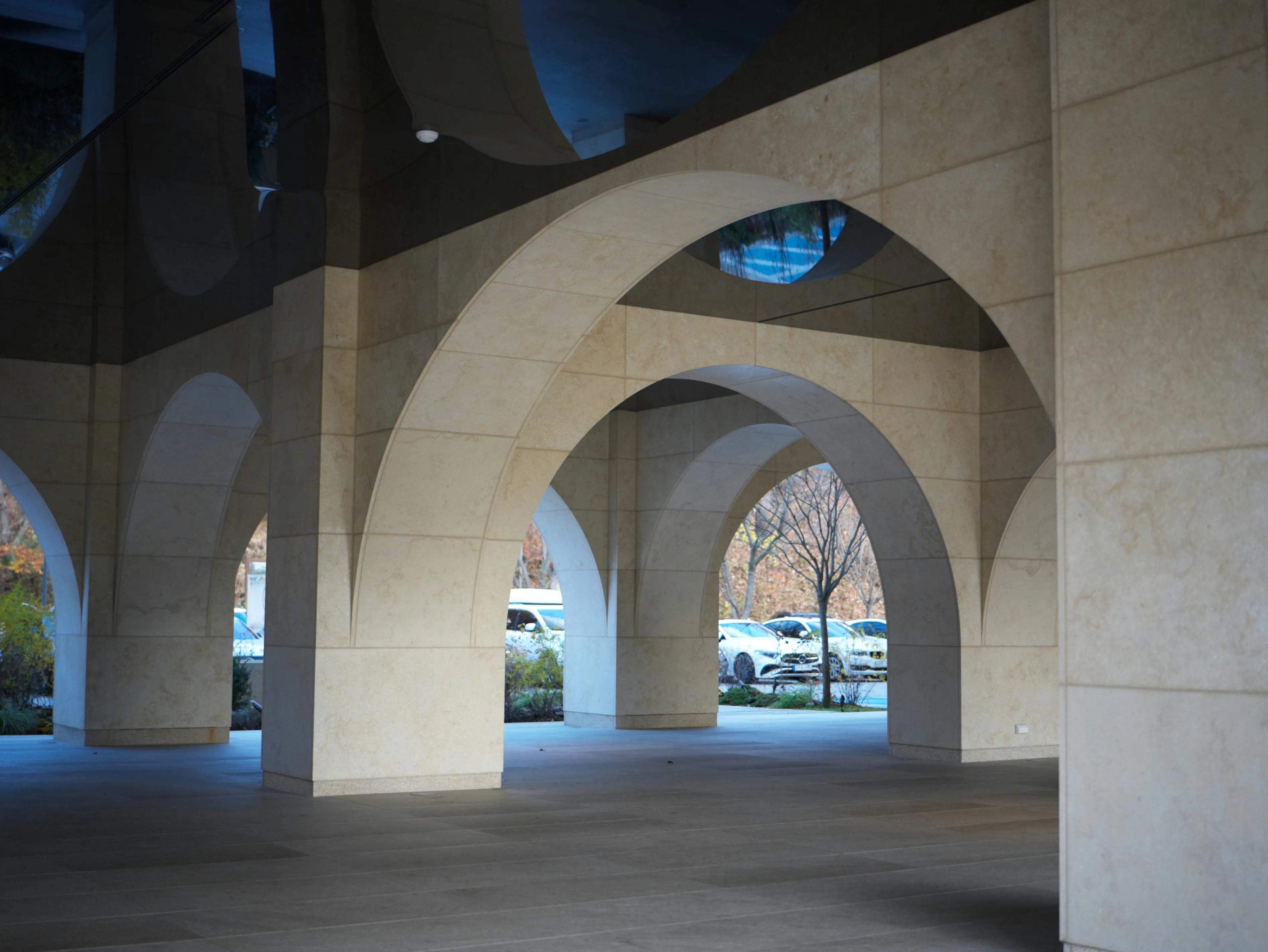 Architectural stone arcade with multiple beige pillars and minimalist arches in a modern building plaza.