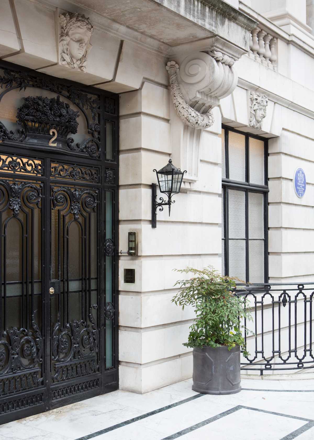 Grand period property entrance showing detailed stone conservation work, ornate wrought iron double doors, a classical portico with carved stone corbels, and an official English Heritage blue plaque on the stone facade.