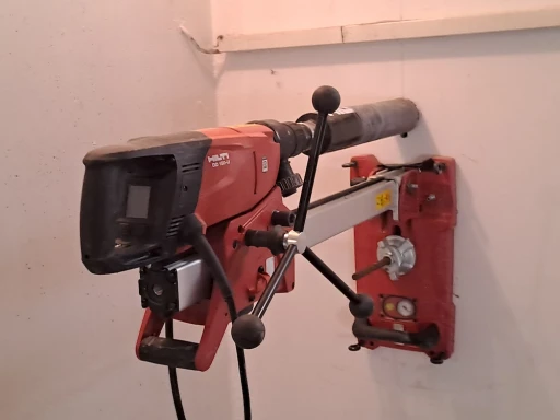 Na zdi je namontovaná červená jádrová vrtačka Hilti. Je určena k vrtání do betonu a jiných tvrdých materiálů.