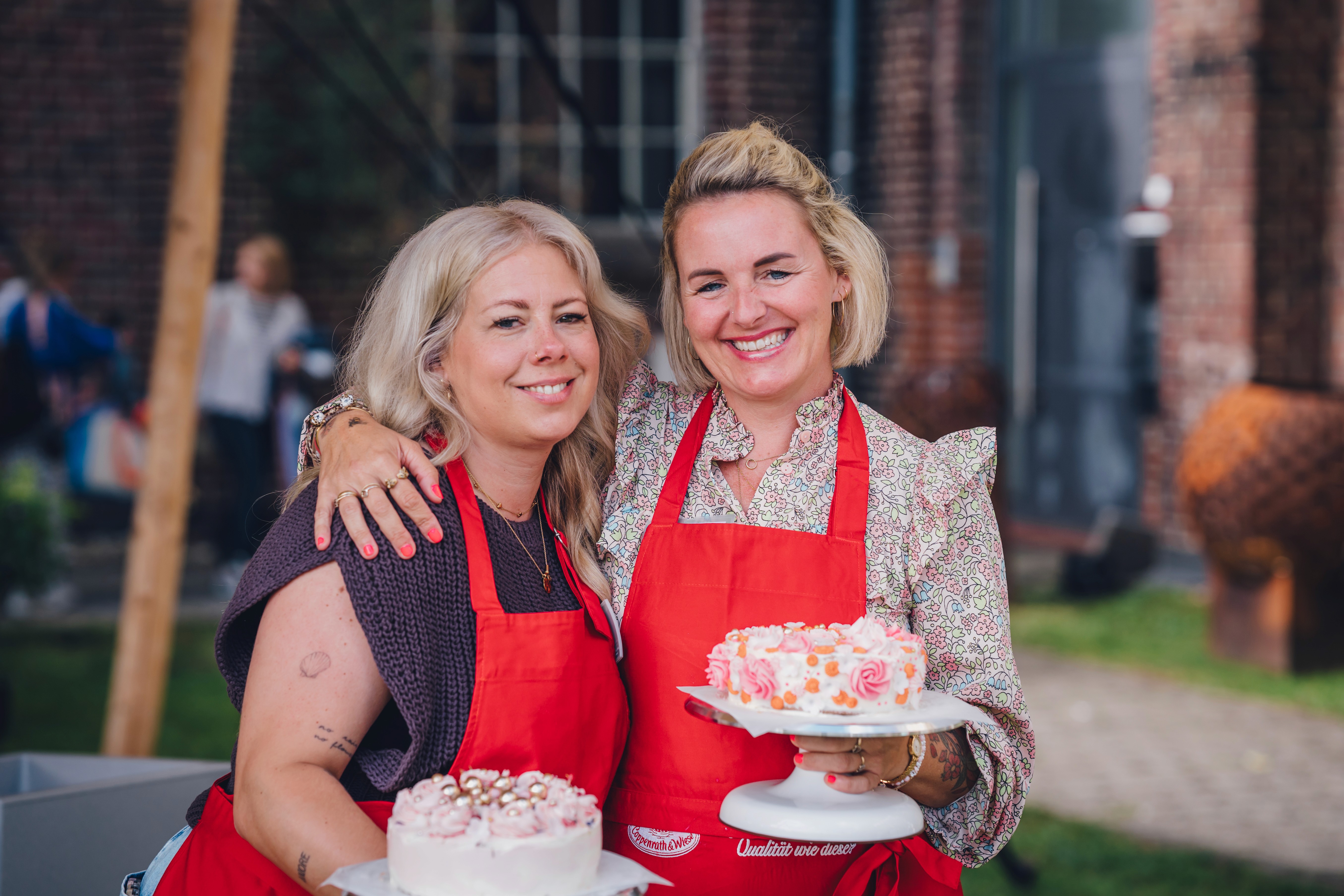 Zwei Frauen präsentieren selbst dekorierte Torten bei einem Backworkshop mit Coppenrath & Wiese im Freien