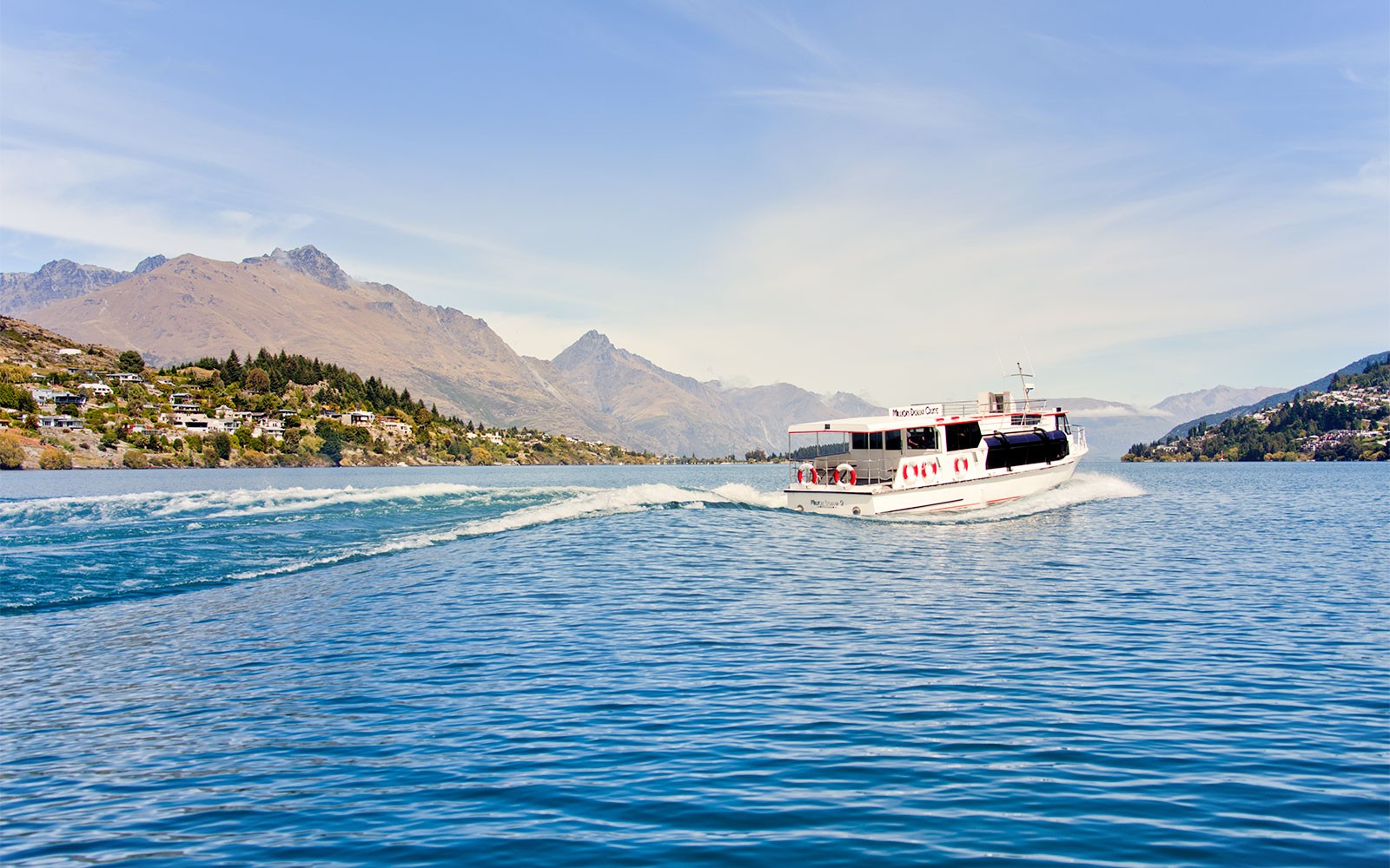 Turistički brod plovi jezerom Wakatipu, uz planine Queenstowna u pozadini.
