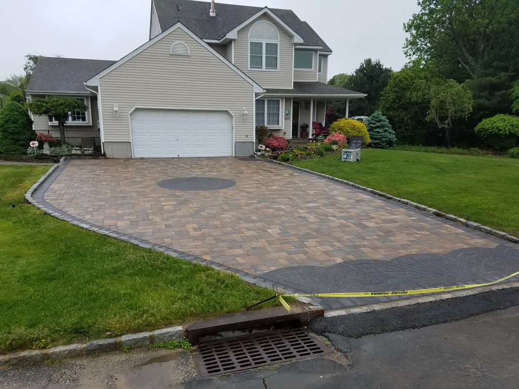 Brown paver driveway with circular inlay in front of two-story home