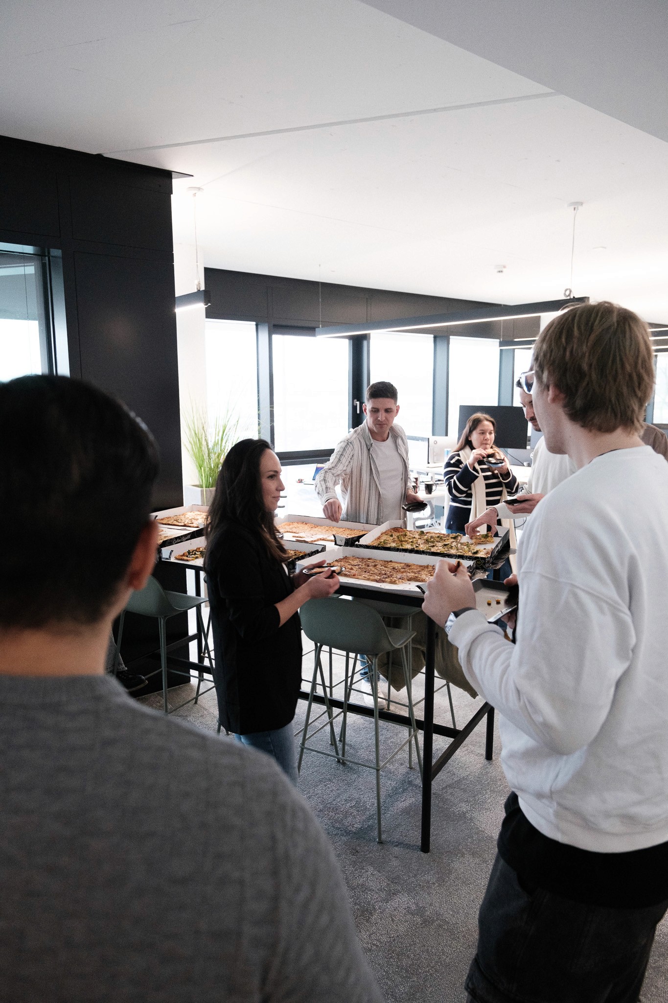 Gemeinsames Mittagessen im enua Büro, verschiedene Mitarbeiter stehen im Kreis und unterhalten sich angeregt.