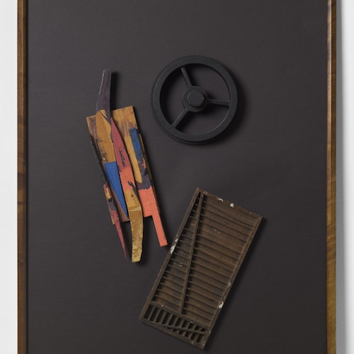 Una cornice nera che mostra una colorata scultura in legno, una ruota nera e una griglia in legno su uno sfondo scuro.