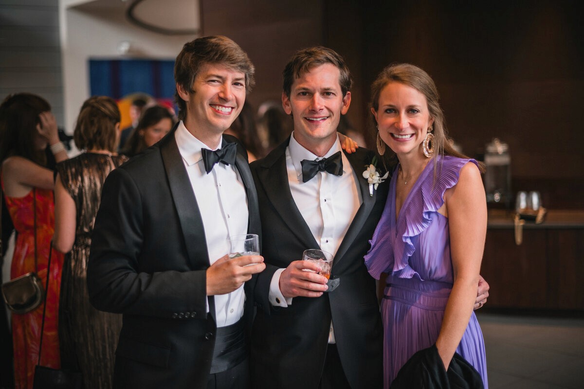 Two guests in black tuxedos posing with a guest in a purple dress at a reception