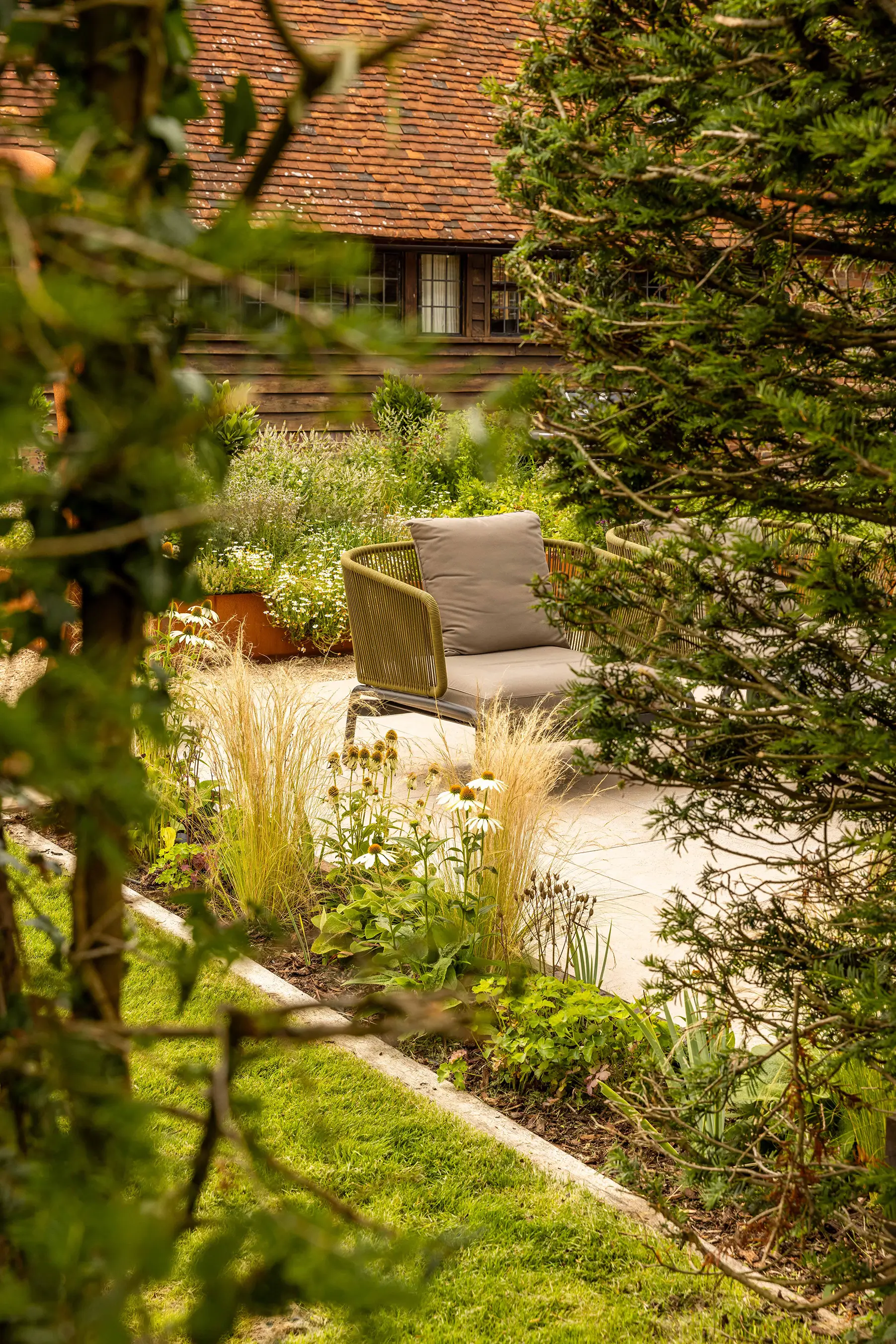 A serene garden scene featuring lush greenery and a stone path, with a blurred background of trees and a structure.