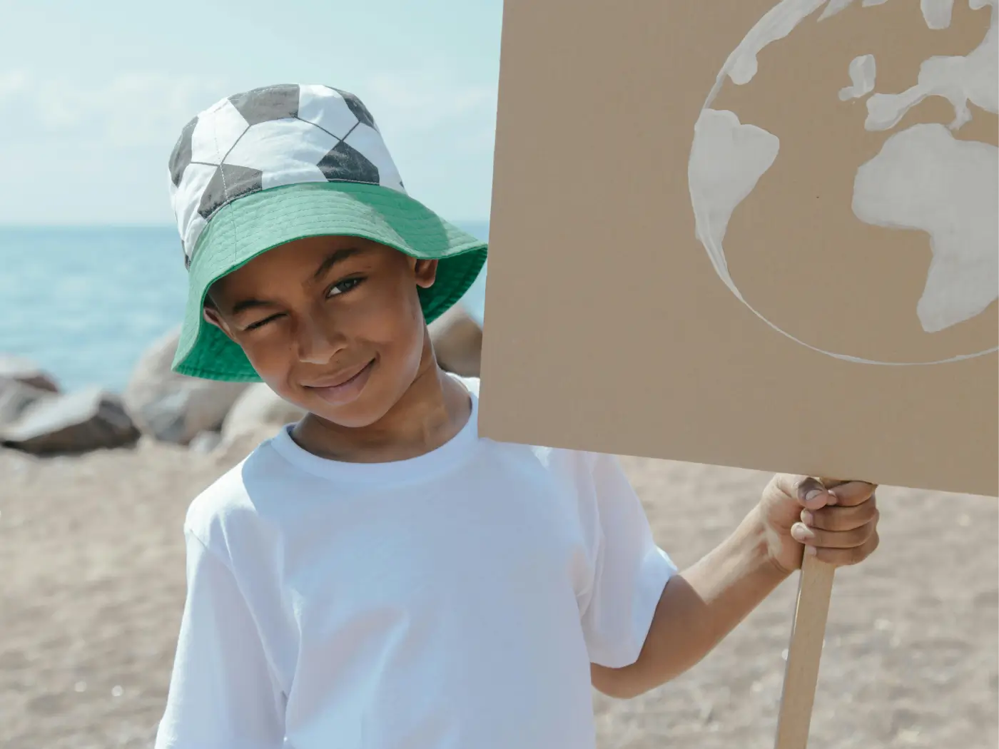 Smiling child holding a sign with the earth symbol on the coast, promoting environmental awareness and protection of planet Earth.