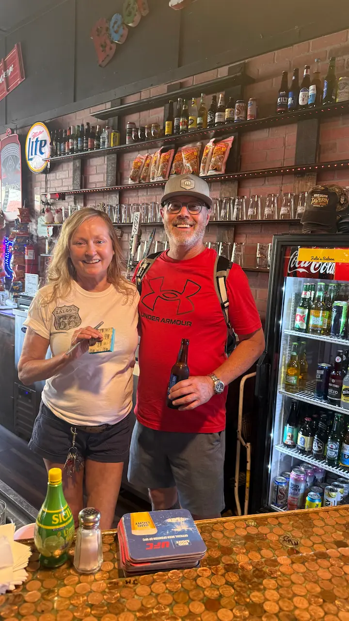 Stu standing behind the bar with Julie, the owner of Judy’s Saloon, inside the historic saloon in Oatman, Arizona.