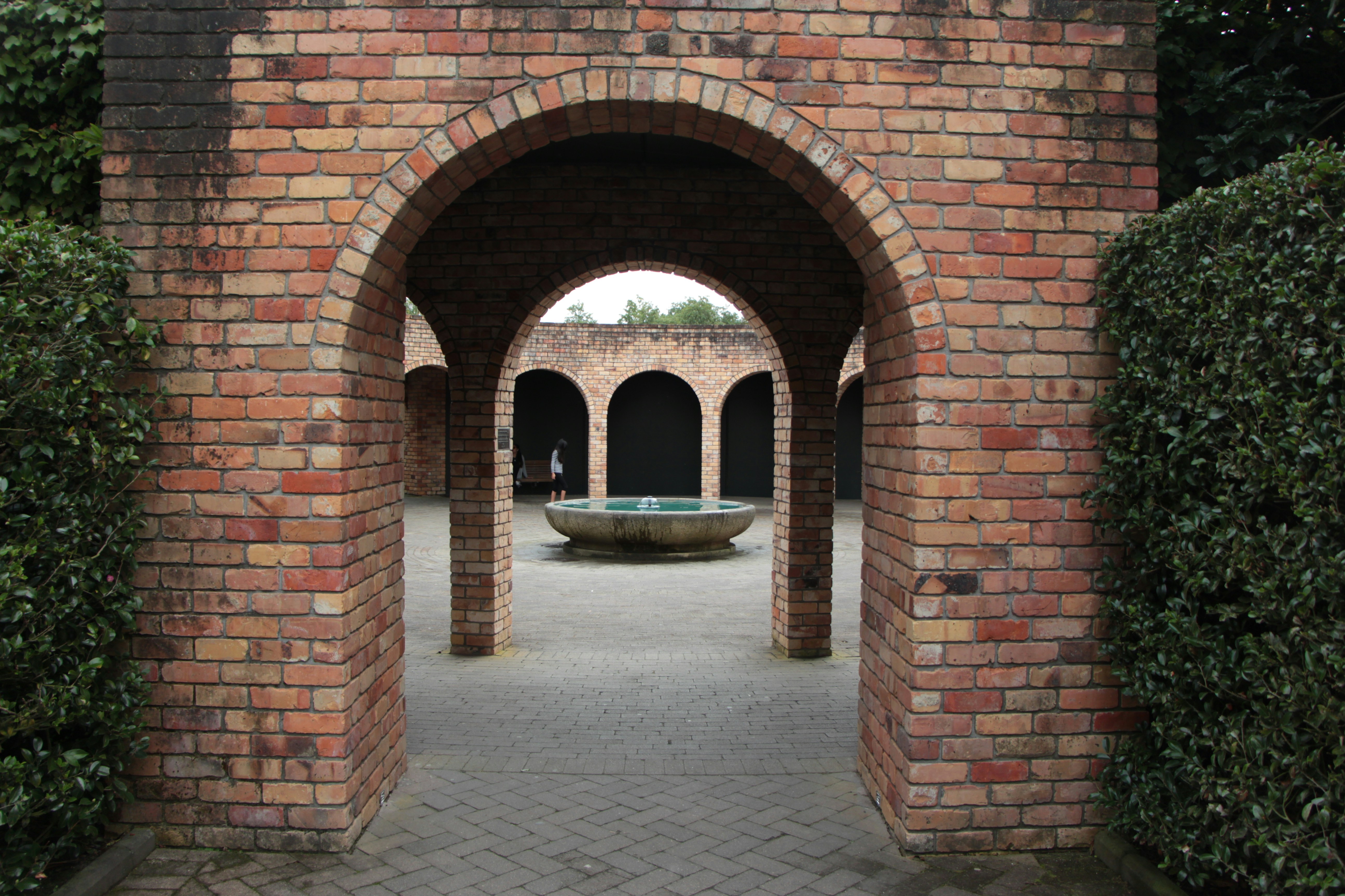 Brick entryway through arches to a circular fountain.