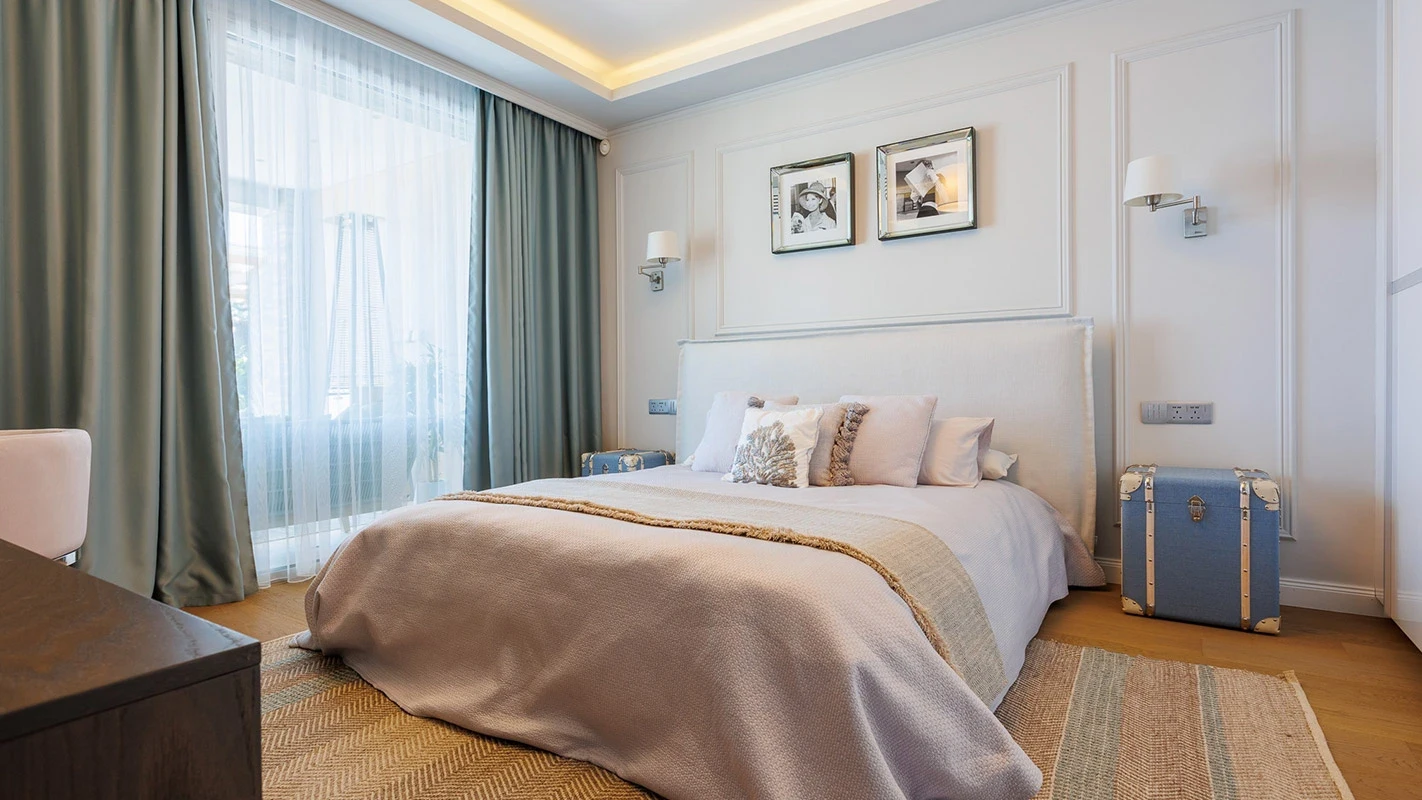 Seafront Residence Limassol serene bedroom with upholstered headboard, layered neutrals, soft green drapery, and vintage trunk accent