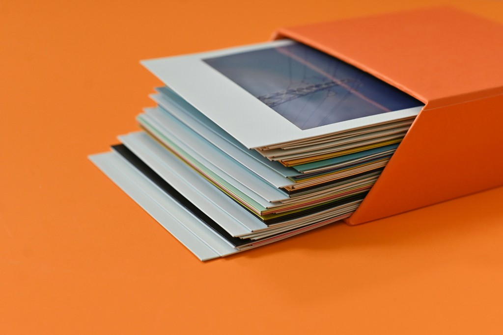 A stack of colorful photo prints partially pulled out of an orange storage box, set against an orange background, evoking a sense of nostalgia and cherished memories.