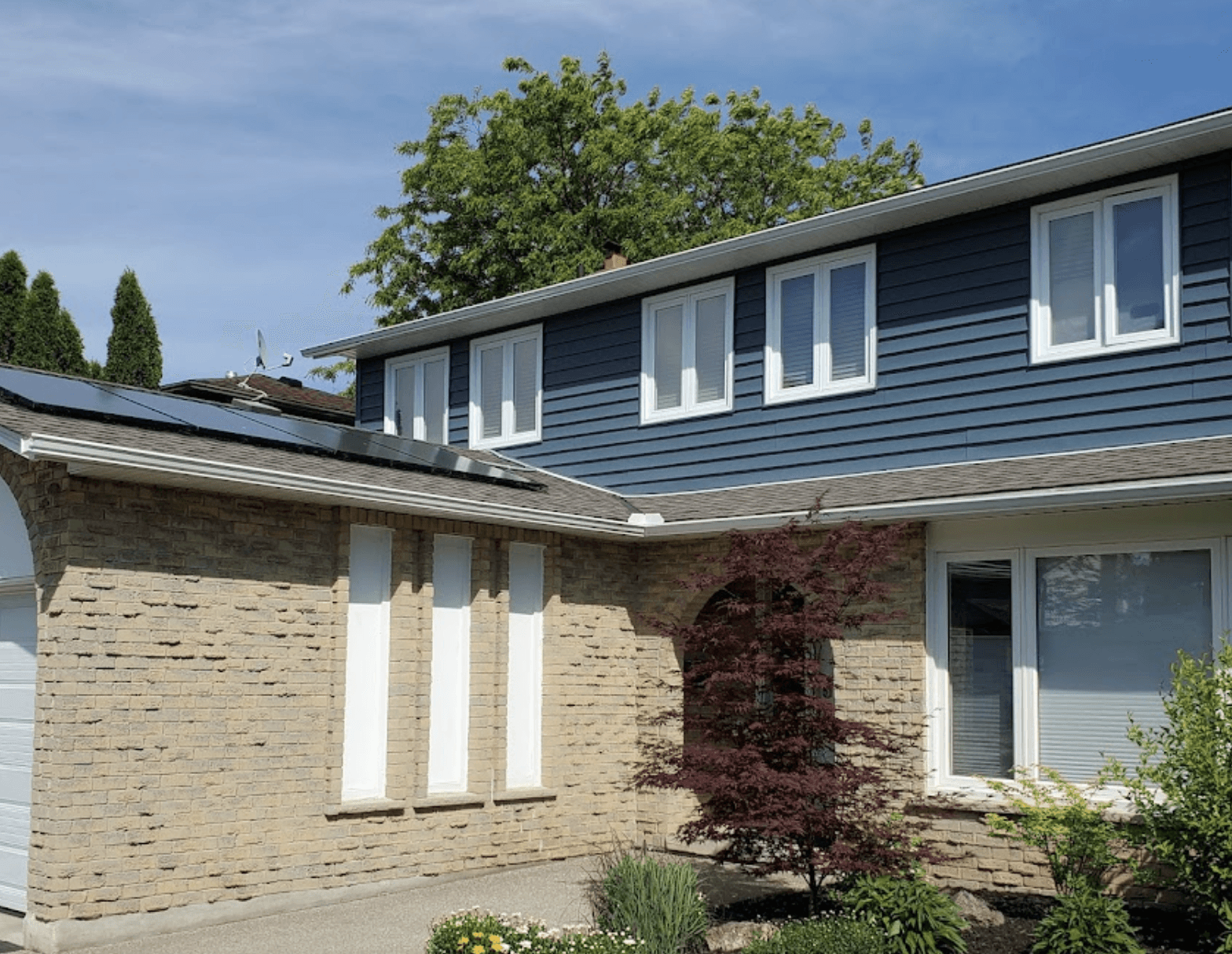 A Modern blue house in southern ontario with grey brick and white windows with solar panels on the roof.