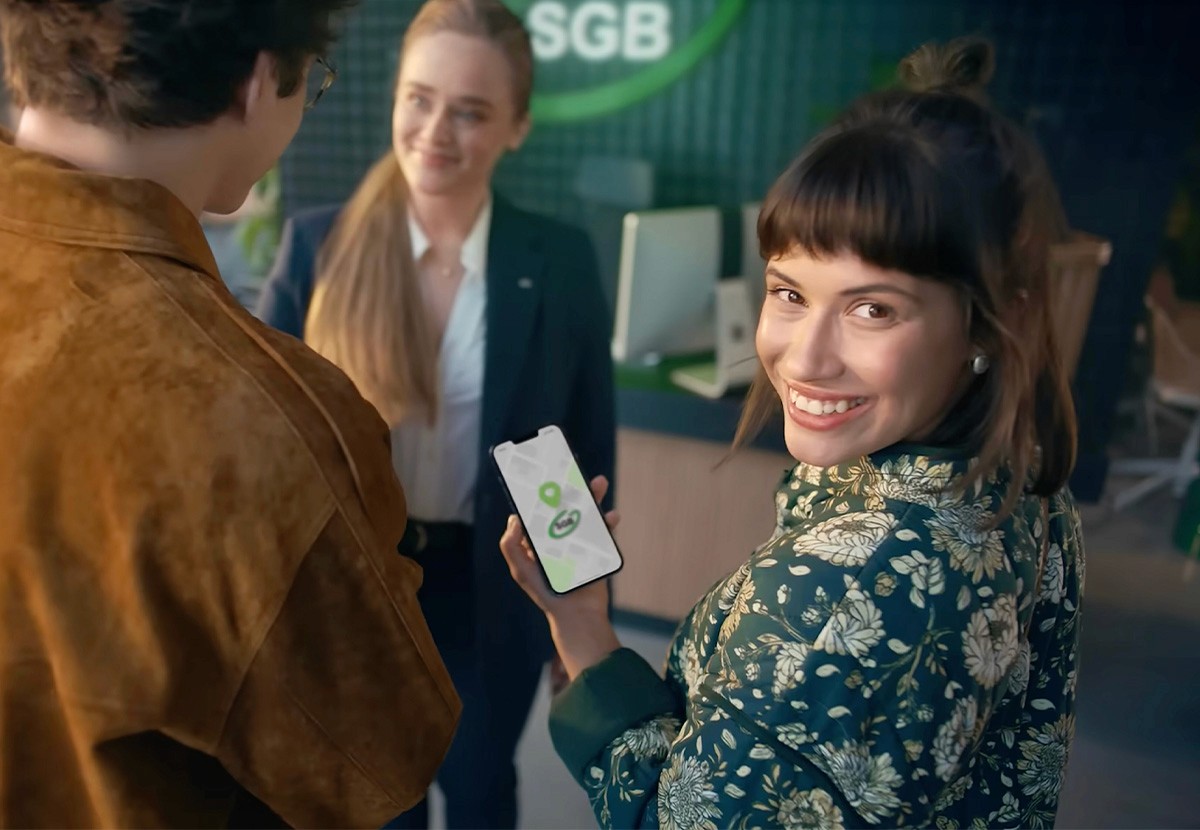 A woman smiles and holds a card while talking to two men in a lively, colorful setting.