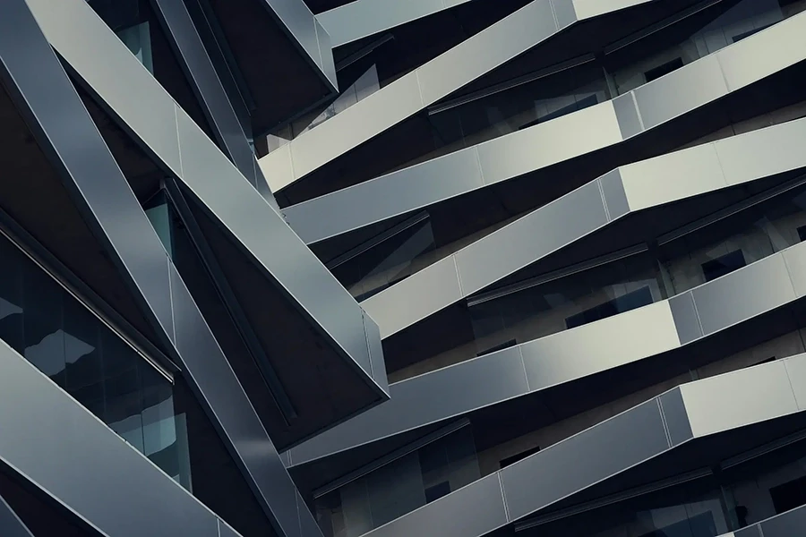 Abstrakte architektonische Nahaufnahme eines modernen Gebäudeprofils mit überlappenden Metall- und Glasplatten, die diagonale geometrische Muster bilden.
