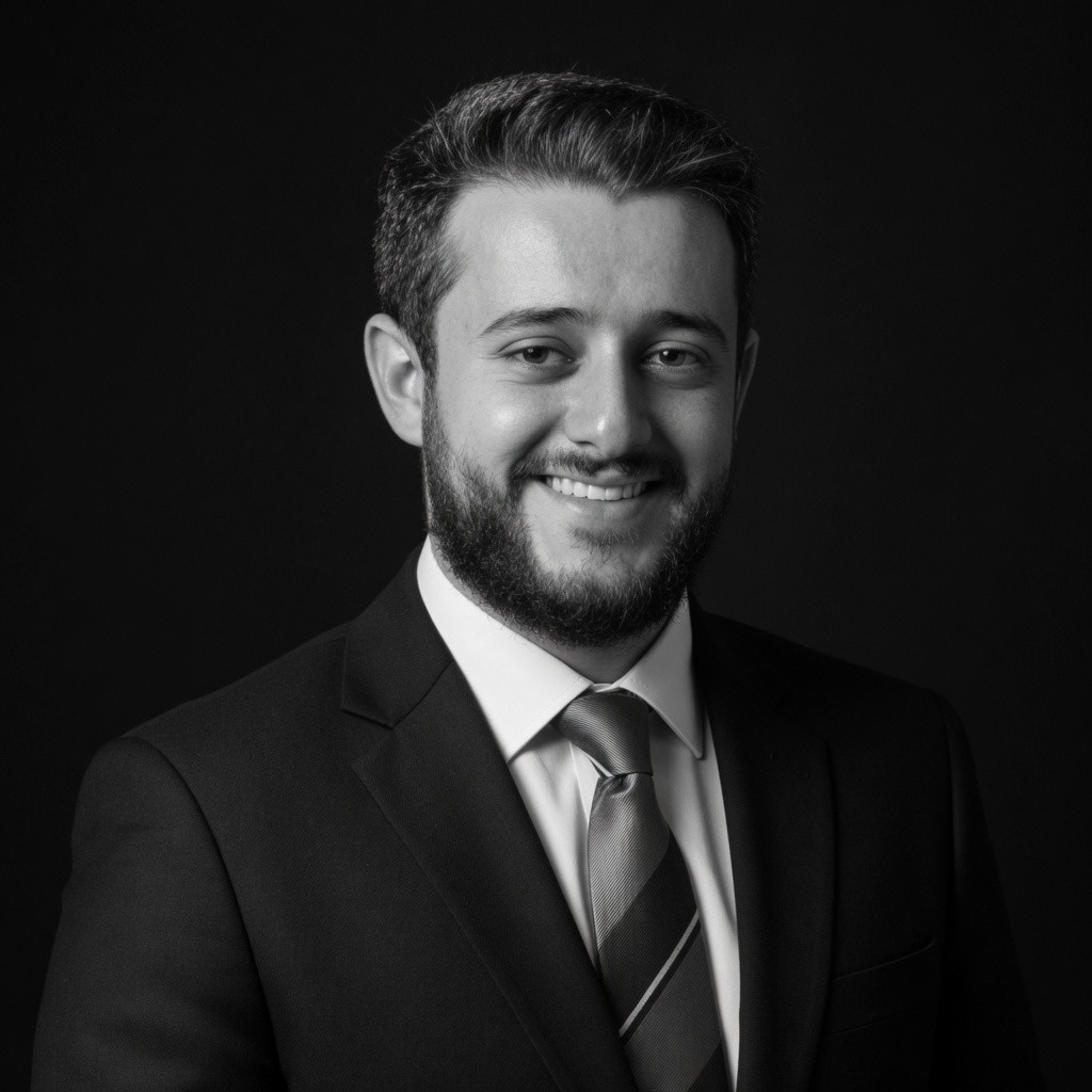Smiling man with light brown hair and stubble, wearing a khaki shirt in natural light