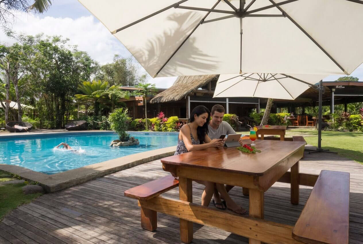 Couples outside under shade umbrellas sitting at a table by the pool in tropical Fiji