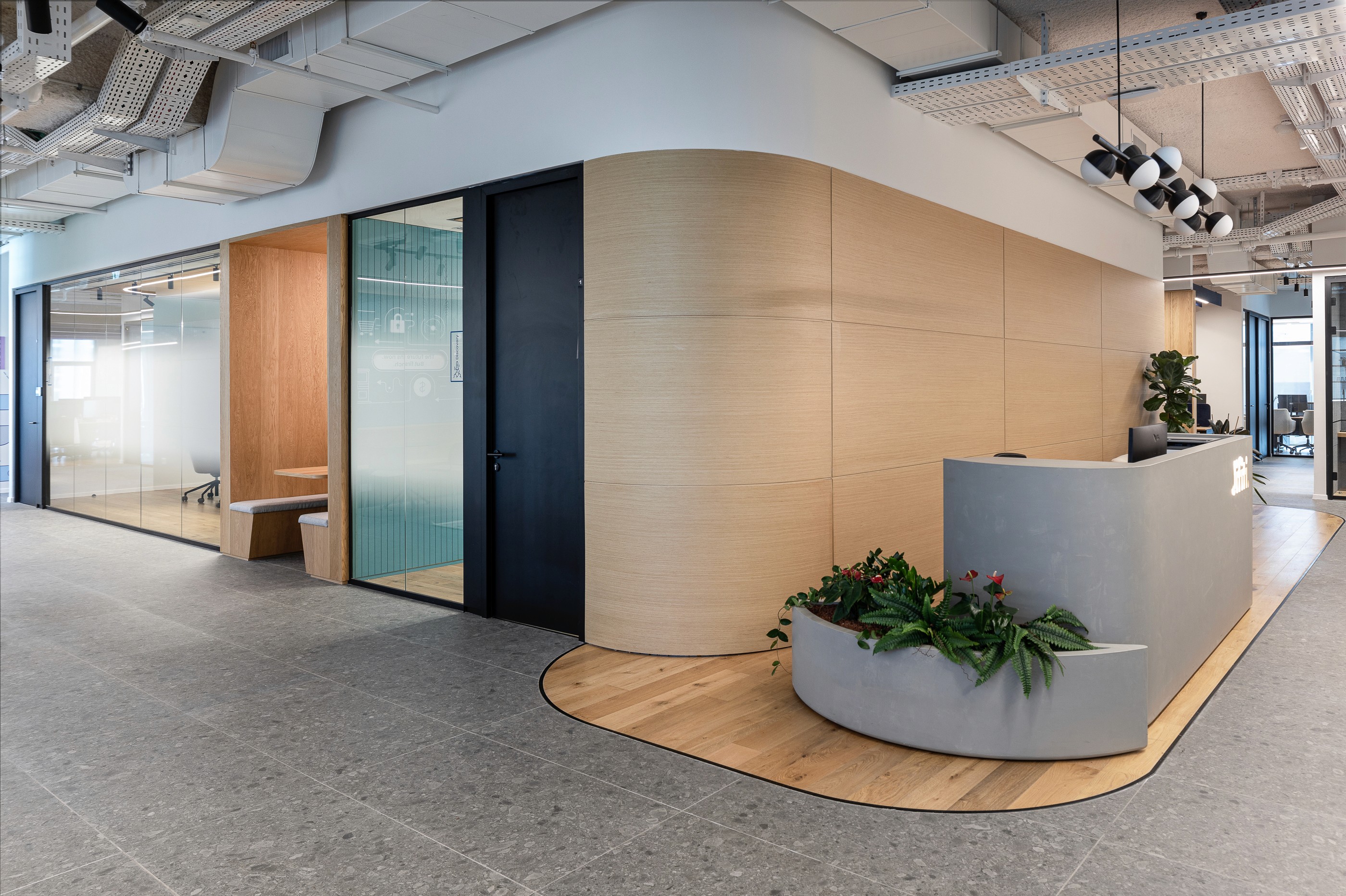 כניסה וקבלה: דלפק בטון אדריכלי בשילוב צמחייה, על רקע קיר חיפוי עץ בקווים מעוגלים (Curved Wood Wall) המכניס חום וזרימה לחלל.