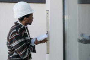 "Construction professional in a hard hat reviewing plans beside a wall-mounted access panel, suggesting site inspection or building compliance checks during a residential project