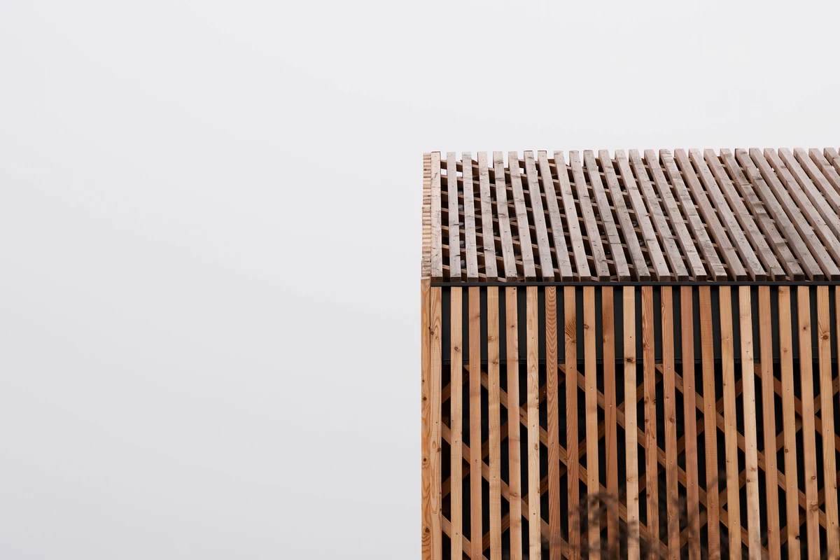 Ecke des lattenverkleideten Baukörpers mit Flachdach vor nebligem grauem Himmel