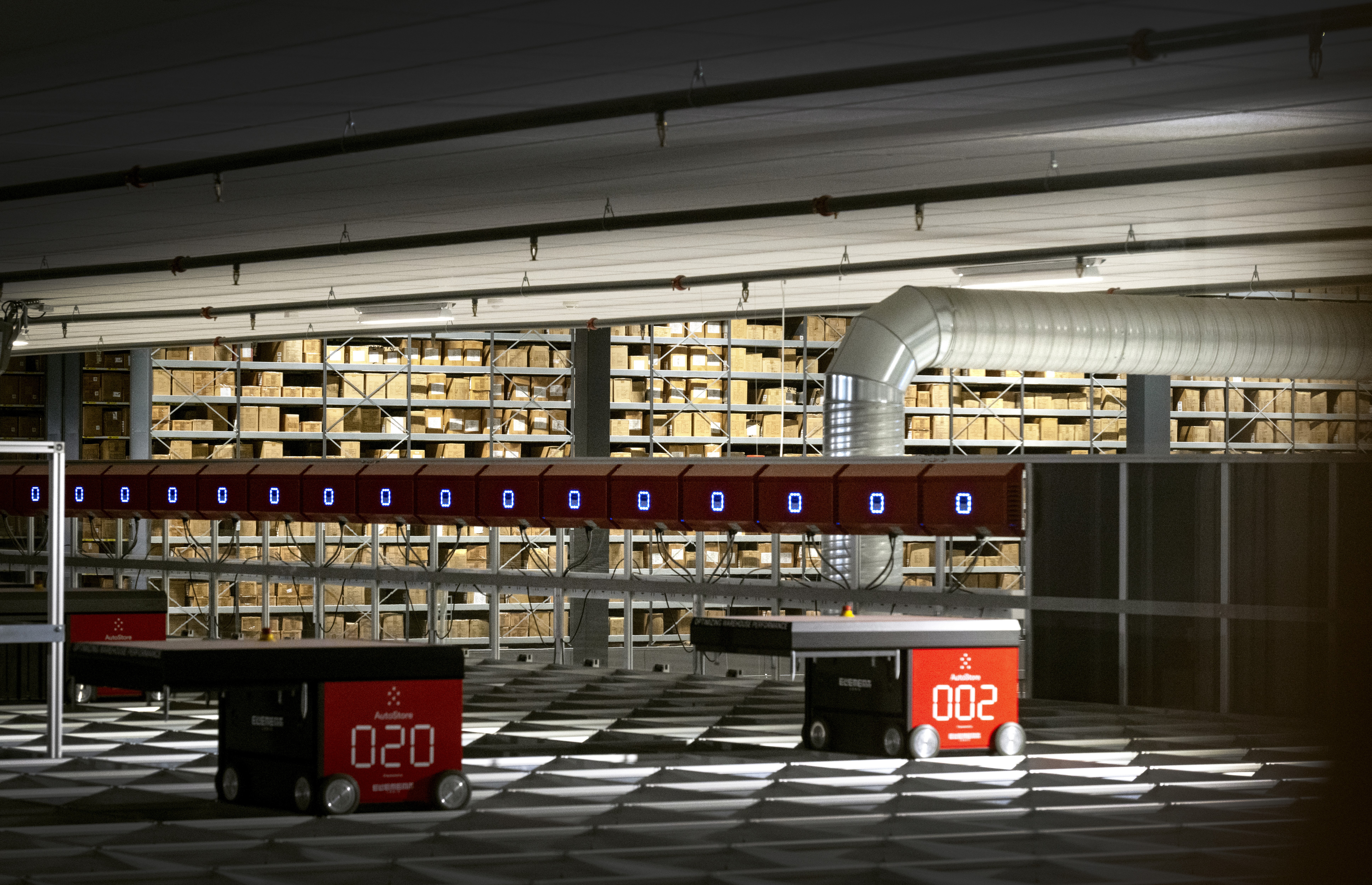 Automatiskt lager med röda fordon som transporterar varor. Hyllor fyllda med förpackningar syns i bakgrunden.