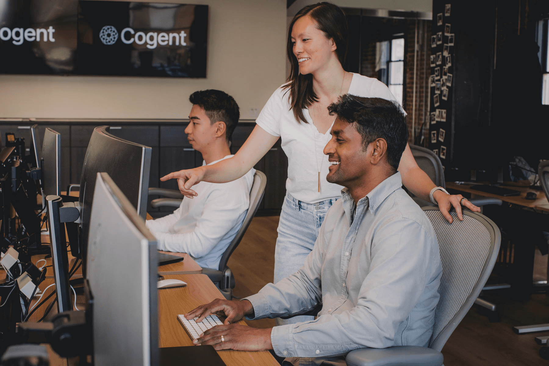 Cogent team members collaborating at computer workstations in a modern office environment.
