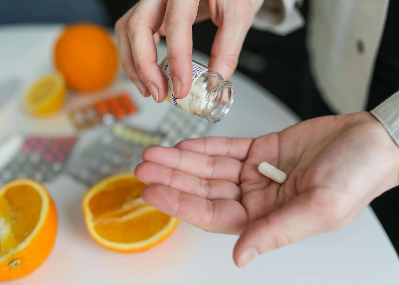 Person taking one supplement with oranges and more supplements in the background