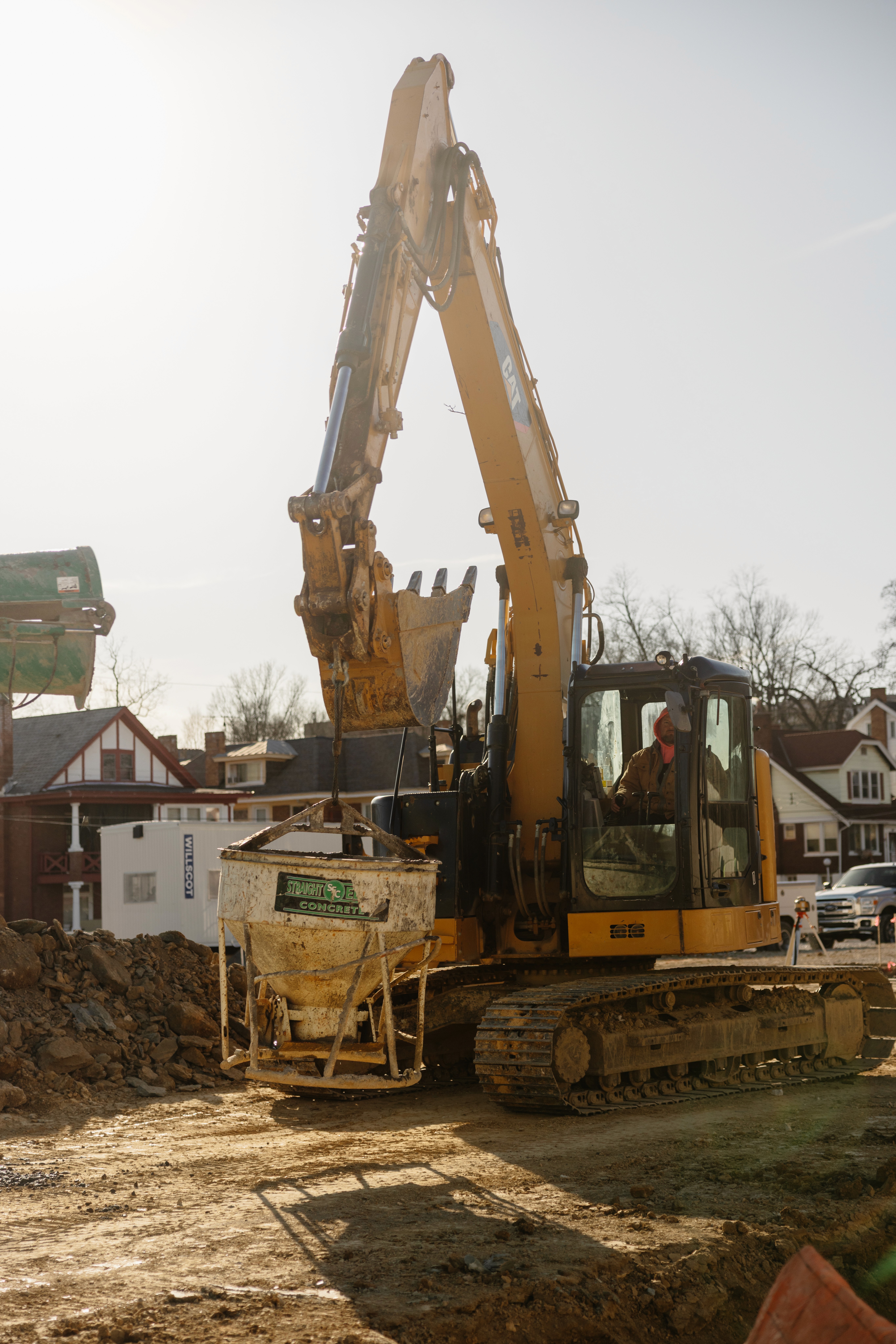 Close-up portrait of a person wearing a gray insulated hooded jacket with the hood up, showing their face framed by the hood against a light background.