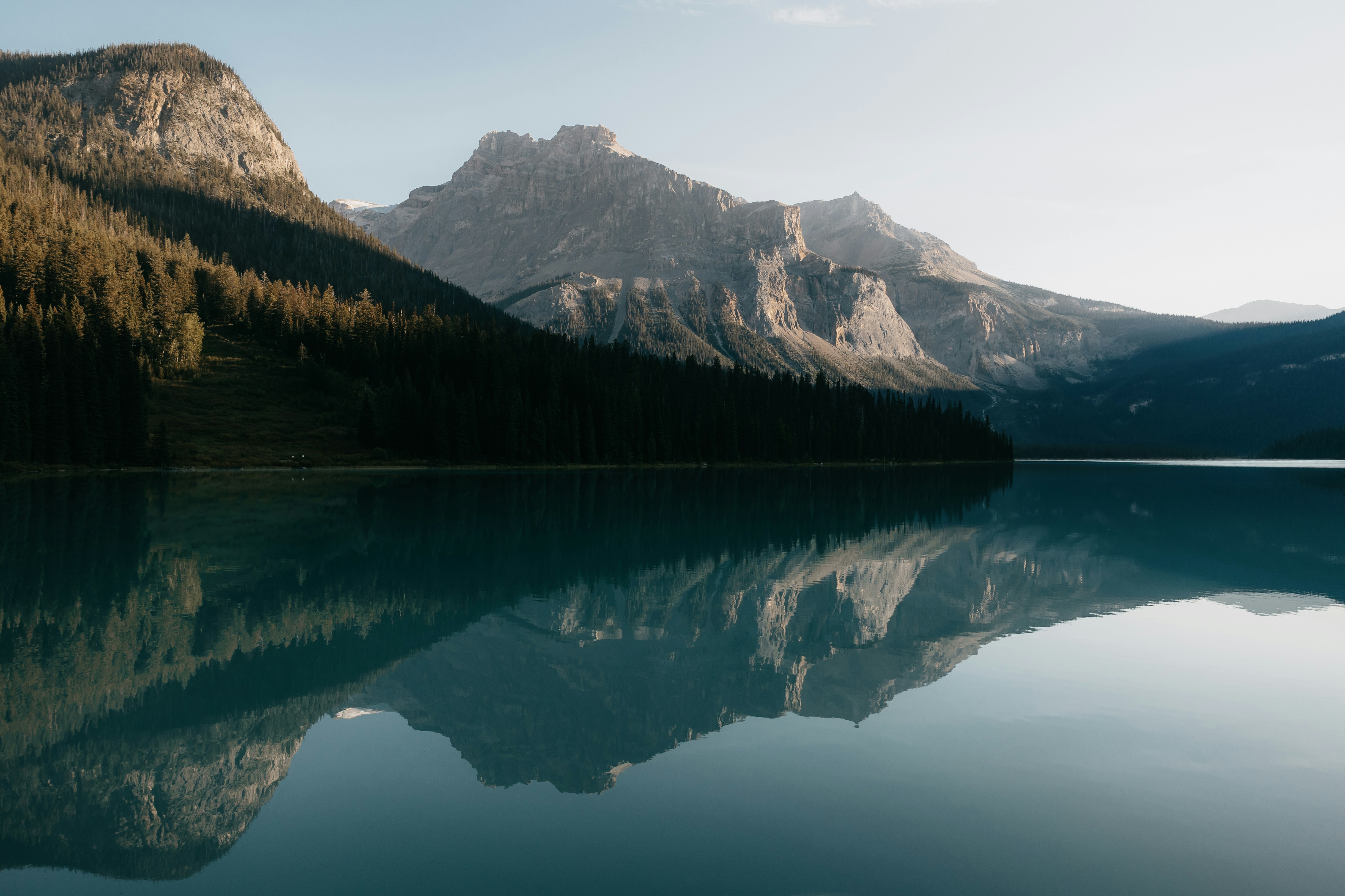 Calm lake reflecting mountains and trees at sunrise
