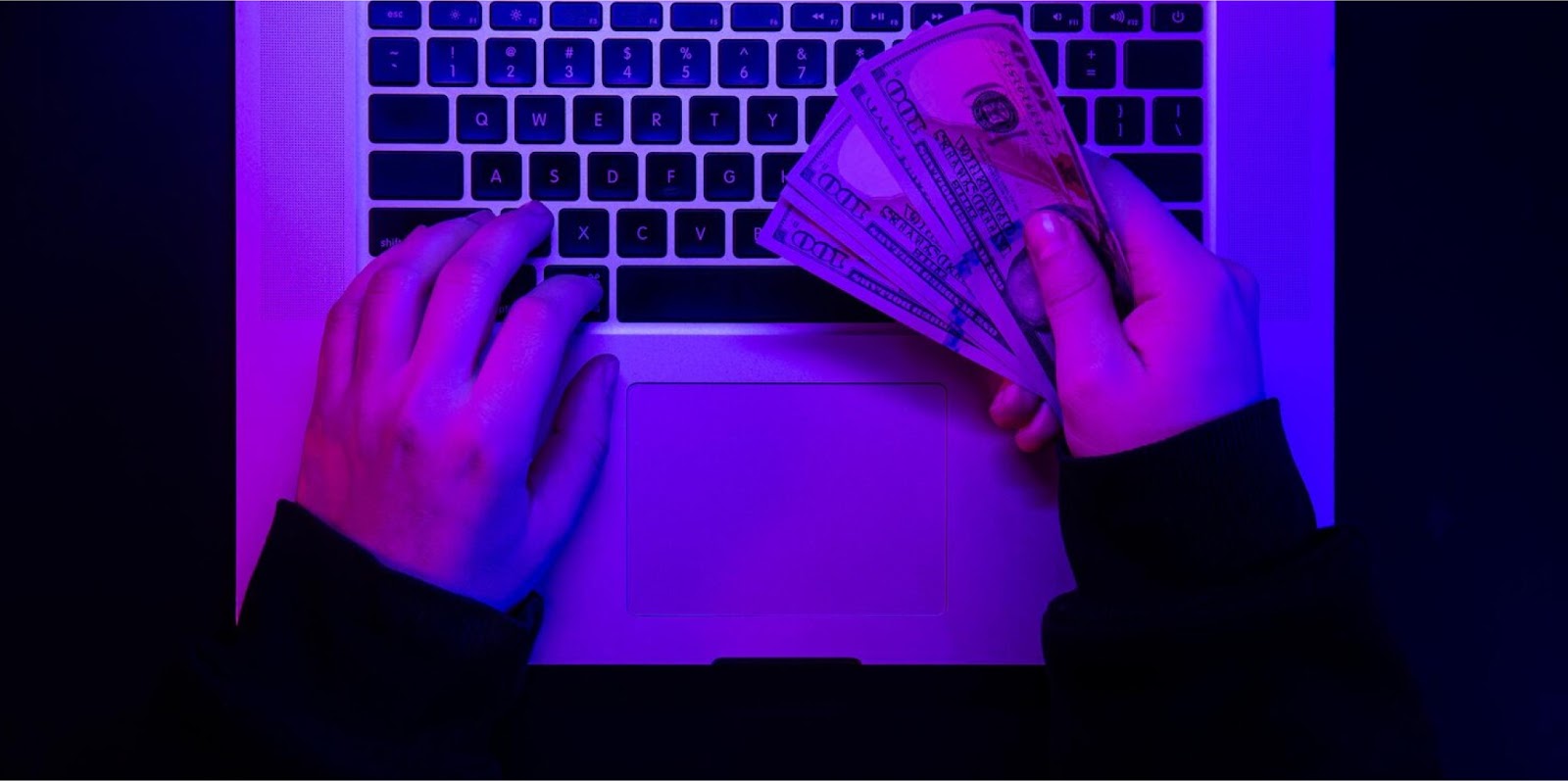 Hände an einer Laptop-Tastatur mit Dollarscheinen in violettem Licht, zu den Kosten von Shopify Plus