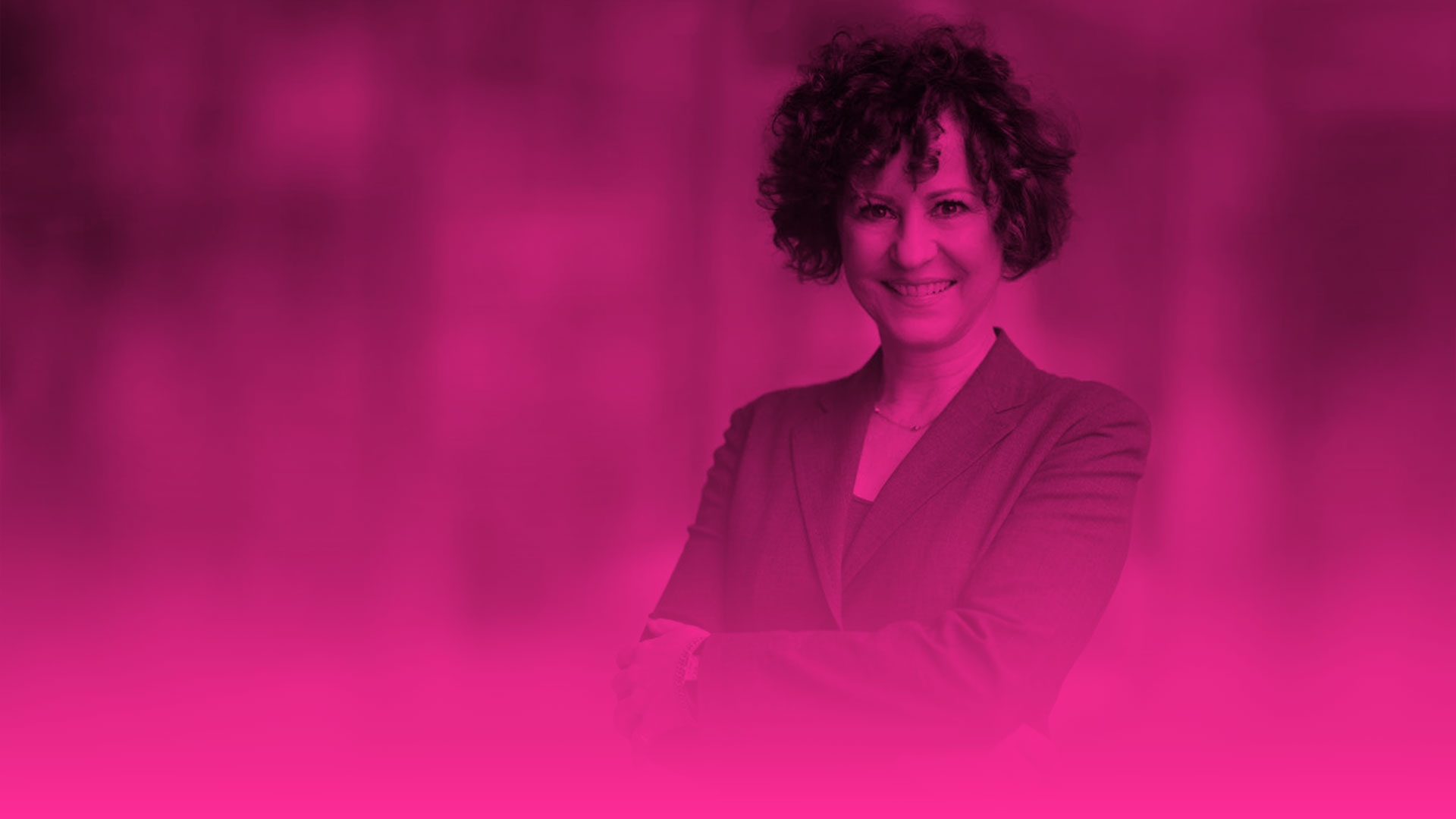 Das Foto zeigt das Porträt einer lächelnden Frau mit kurzen Locken, die direkt in die Kamera blickt. Sie trägt einen Blazer und hat die Arme selbstbewusst vor dem Körper verschränkt. (Es handelt sich um das gleiche Ausgangsfoto wie bei einem der vorherigen Bilder). Das gesamte Bild ist stark verfremdet und komplett in einem intensiven Magenta-Ton (Pink) eingefärbt. Wie bei den beiden vorherigen Porträts dieser Reihe geht die untere Bildhälfte fließend in eine durchgehende, leuchtend pinke Farbfläche über. Der unscharfe Hintergrund lässt die Umrisse einer modernen Umgebung erahnen.