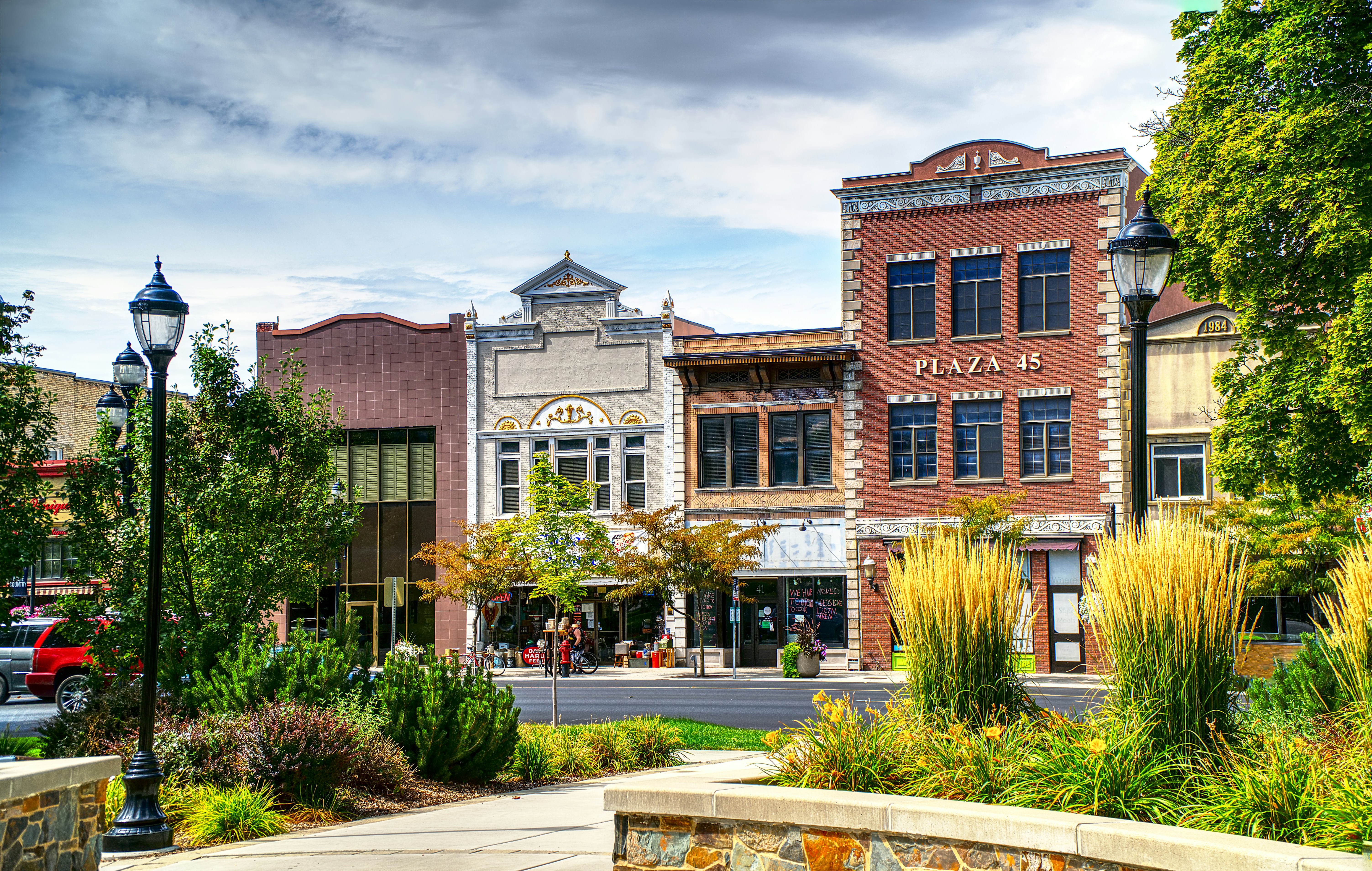 A view of a charming town square featuring brick buildings, greenery, and a partly cloudy sky. North Logan Utah