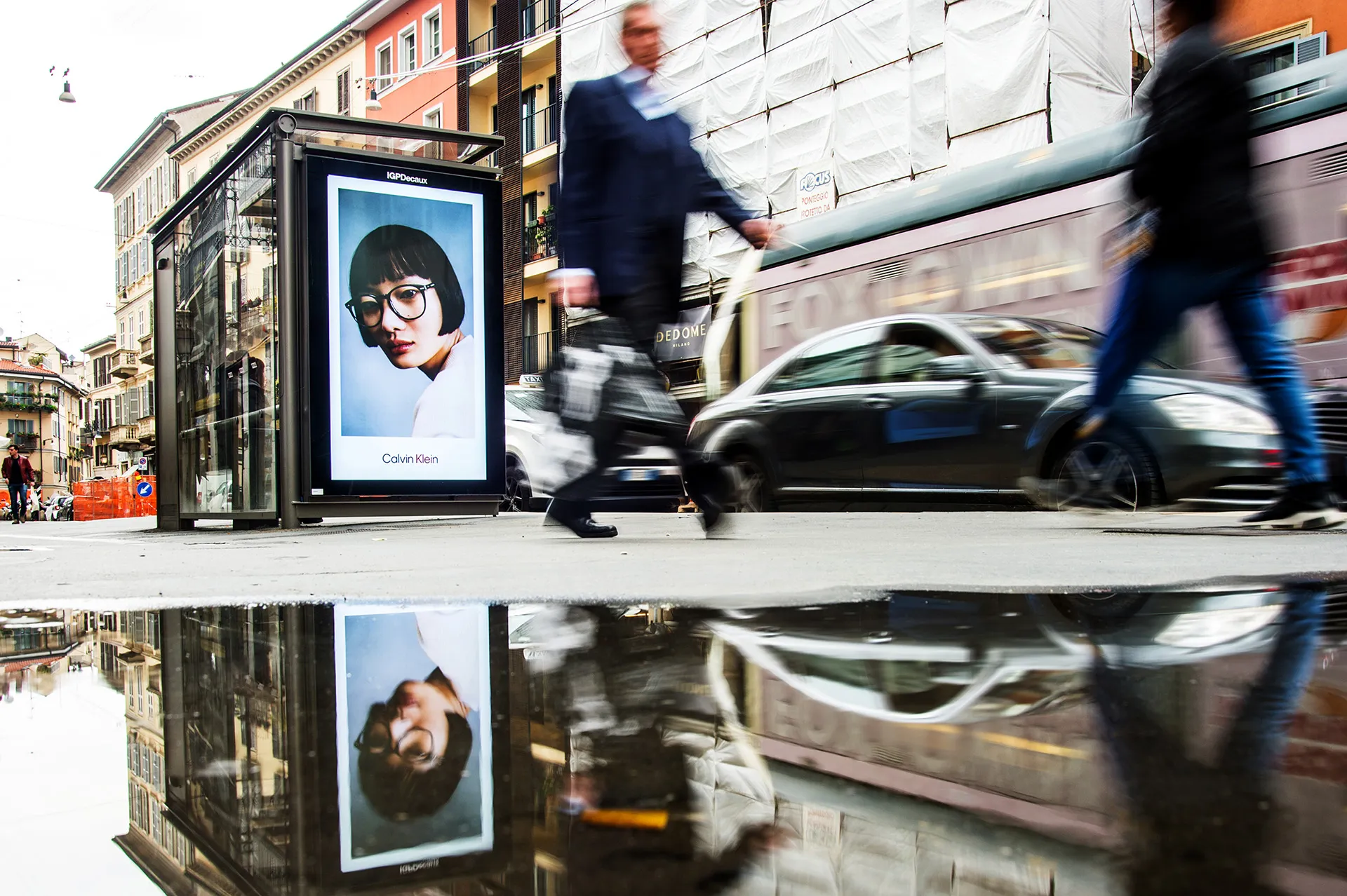 a man walking down a street past a large poster